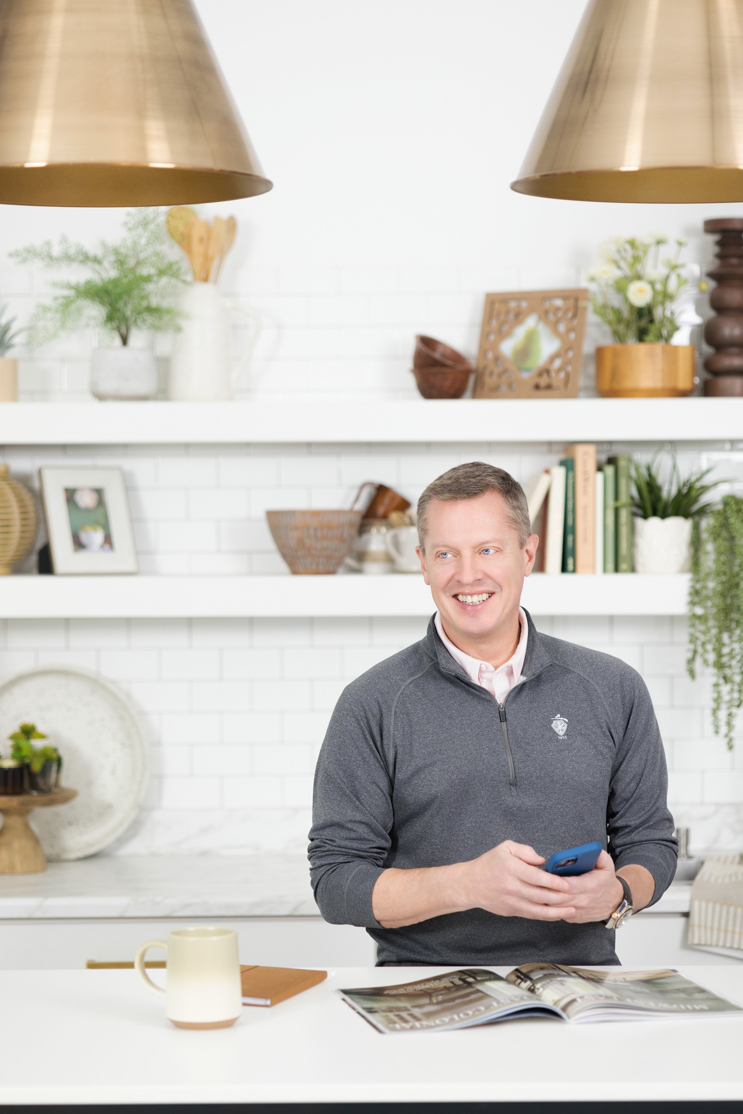 Man in kitchen or library at standing desk, looking at someone out of frame and smiling.  lifestyle headshot by tammy brice in minneapolis