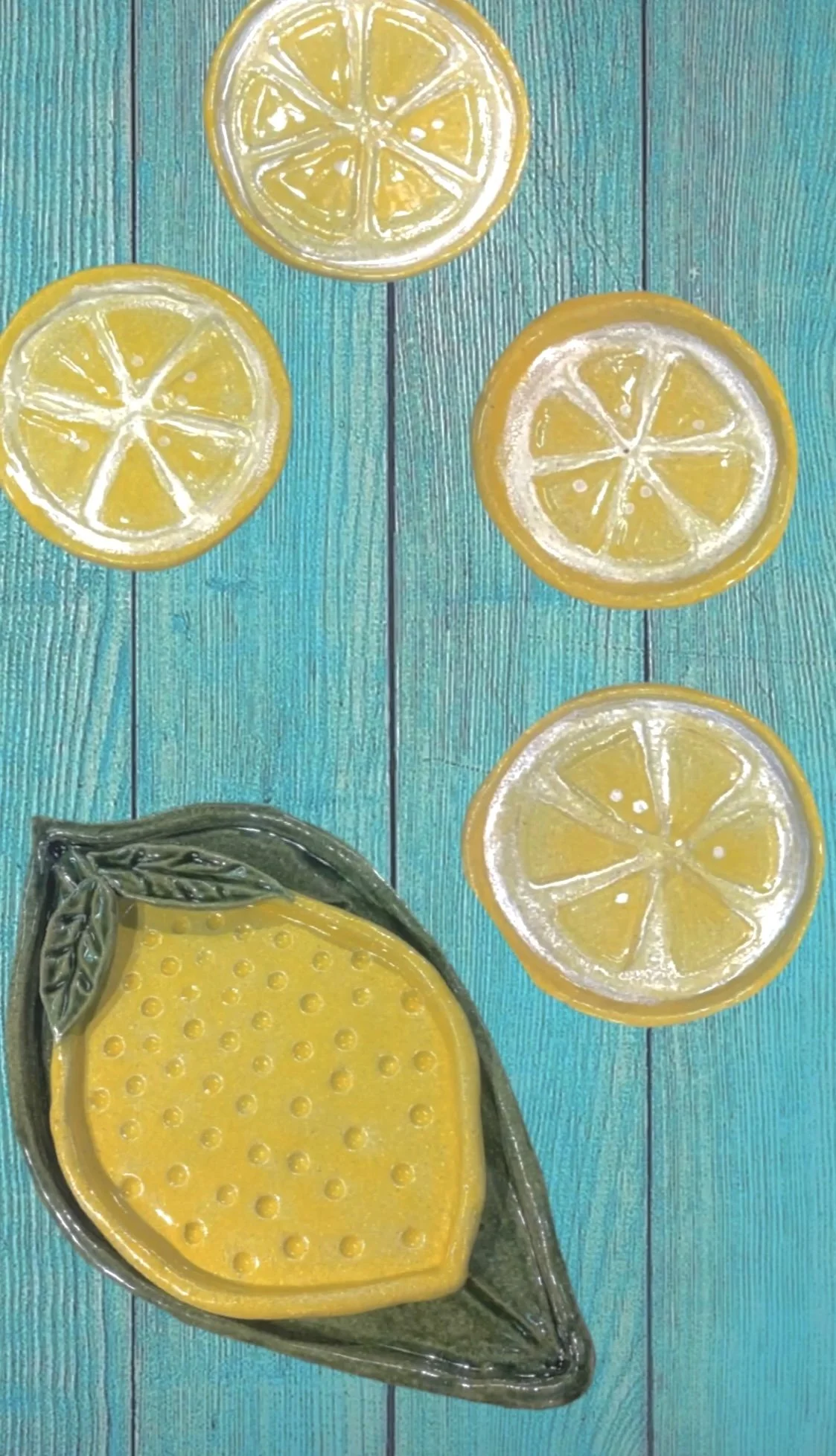 Set of lemonade-themed platters on a turquoise wooden surface, including four round lemon-slice-shaped plates with a lemon designed platter and green leaf platter.