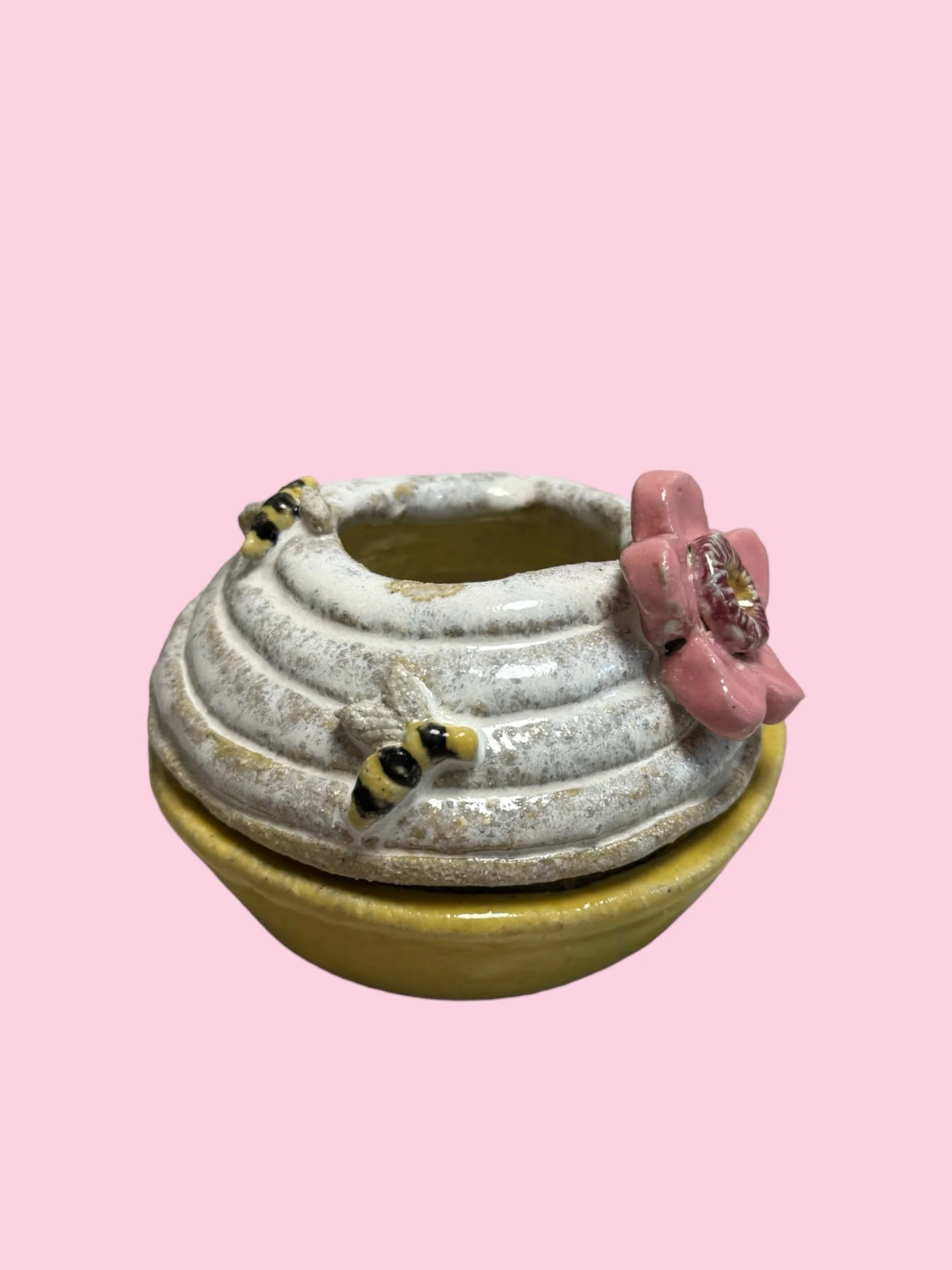 Ceramic bowl with a textured top, decorated with honey bees and a pink flower, set against a pink background.