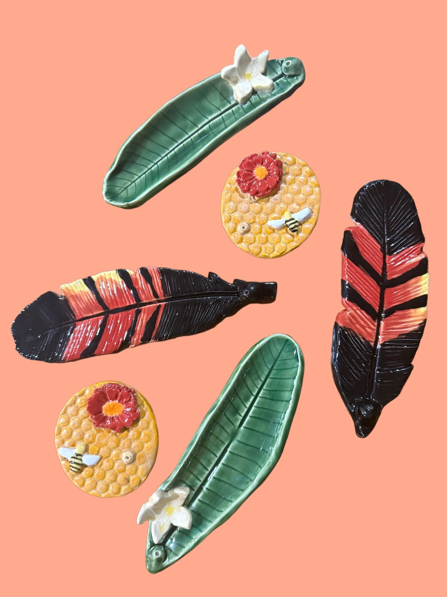 Decorative ceramic incense holders shaped like leaves, honeycomb, and flowers with bees, displayed on a peach background.