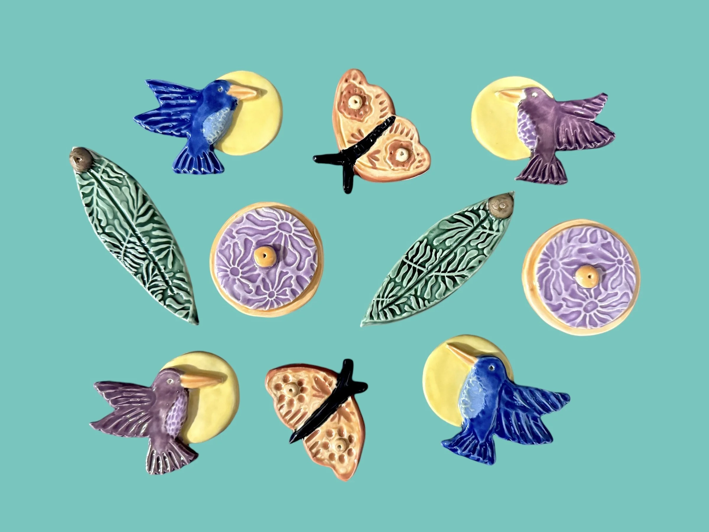 Colorful ceramic dishes with patterns, decorative birds, and butterfly-shaped objects on a teal background.
