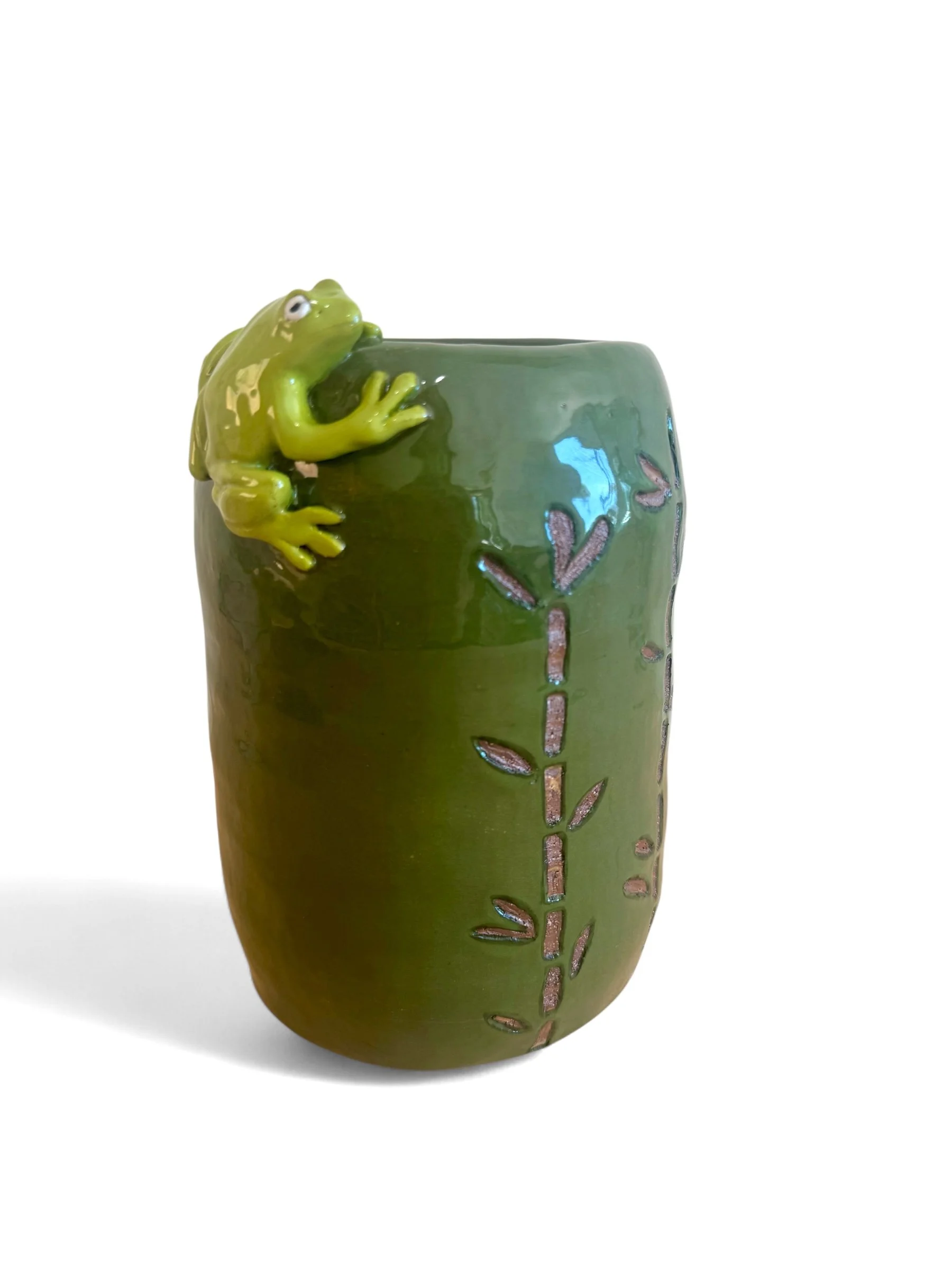 A green ceramic mug with decorative pinkish-brown leaves and a playful green frog figurine climbing over its rim.