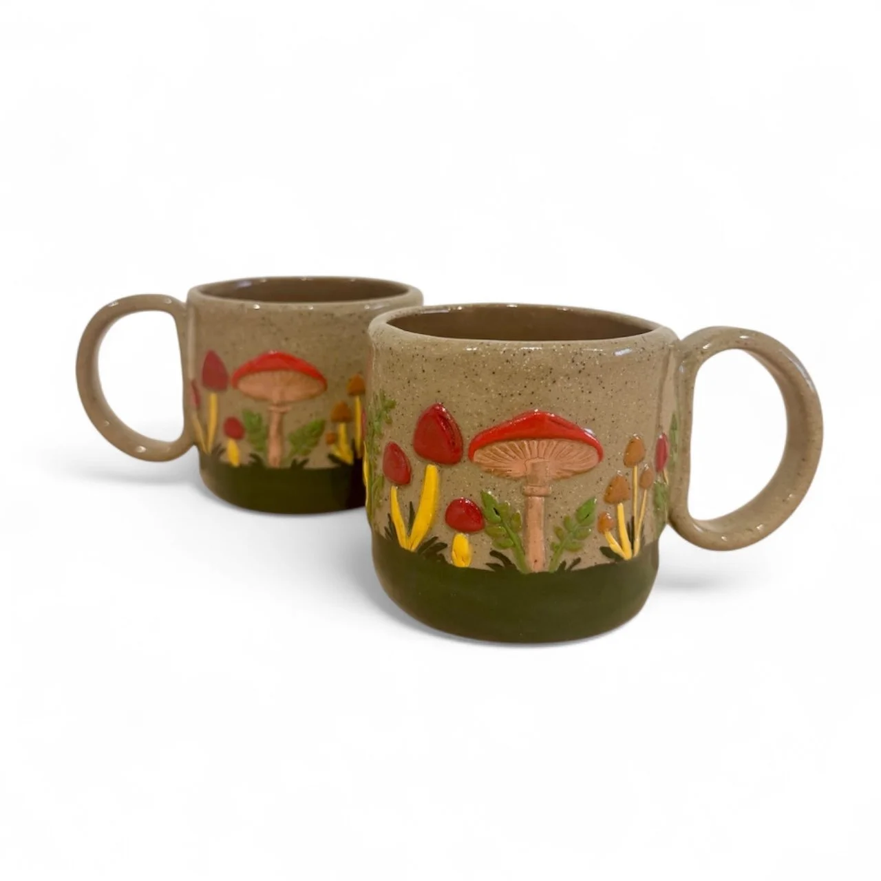 Two ceramic mugs with mushroom and plant designs, placed against a white background.