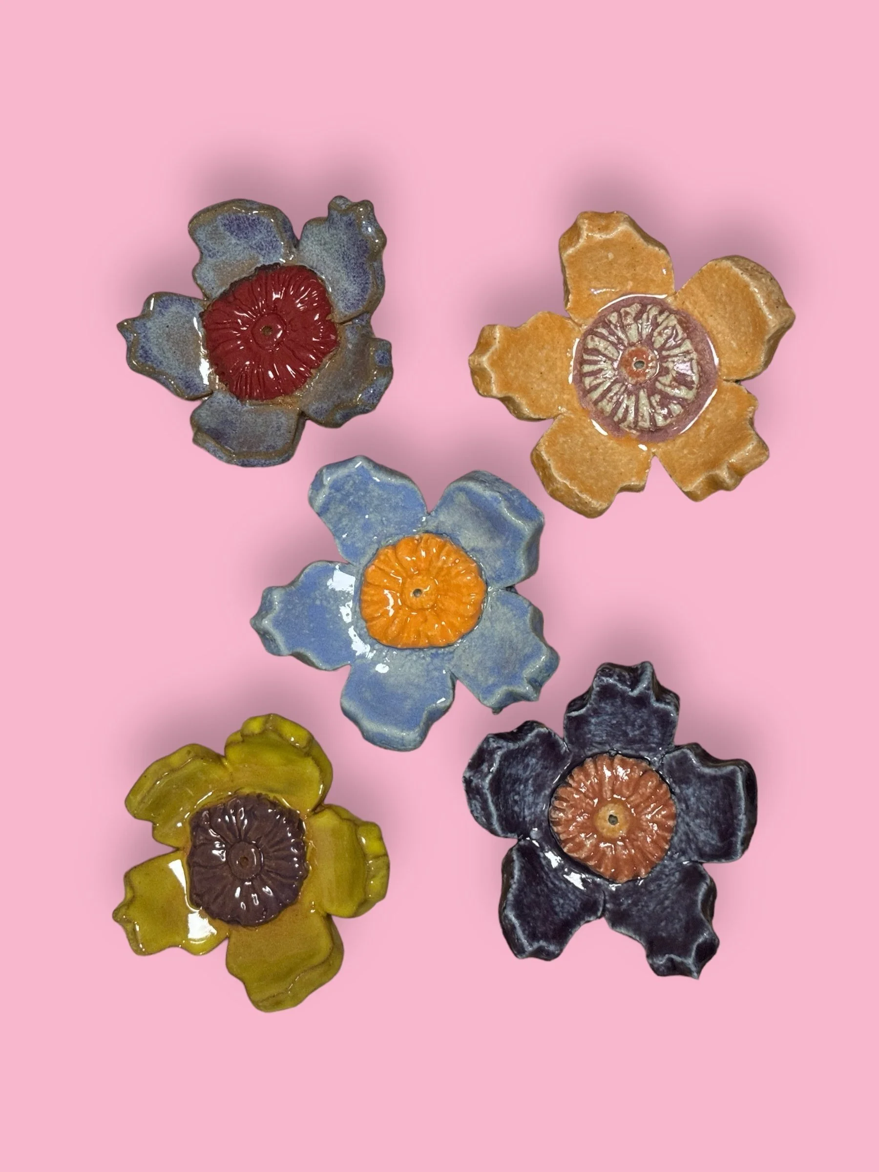 Colorful ceramic flower-shaped objects with a round, textured center, placed on a pink background.