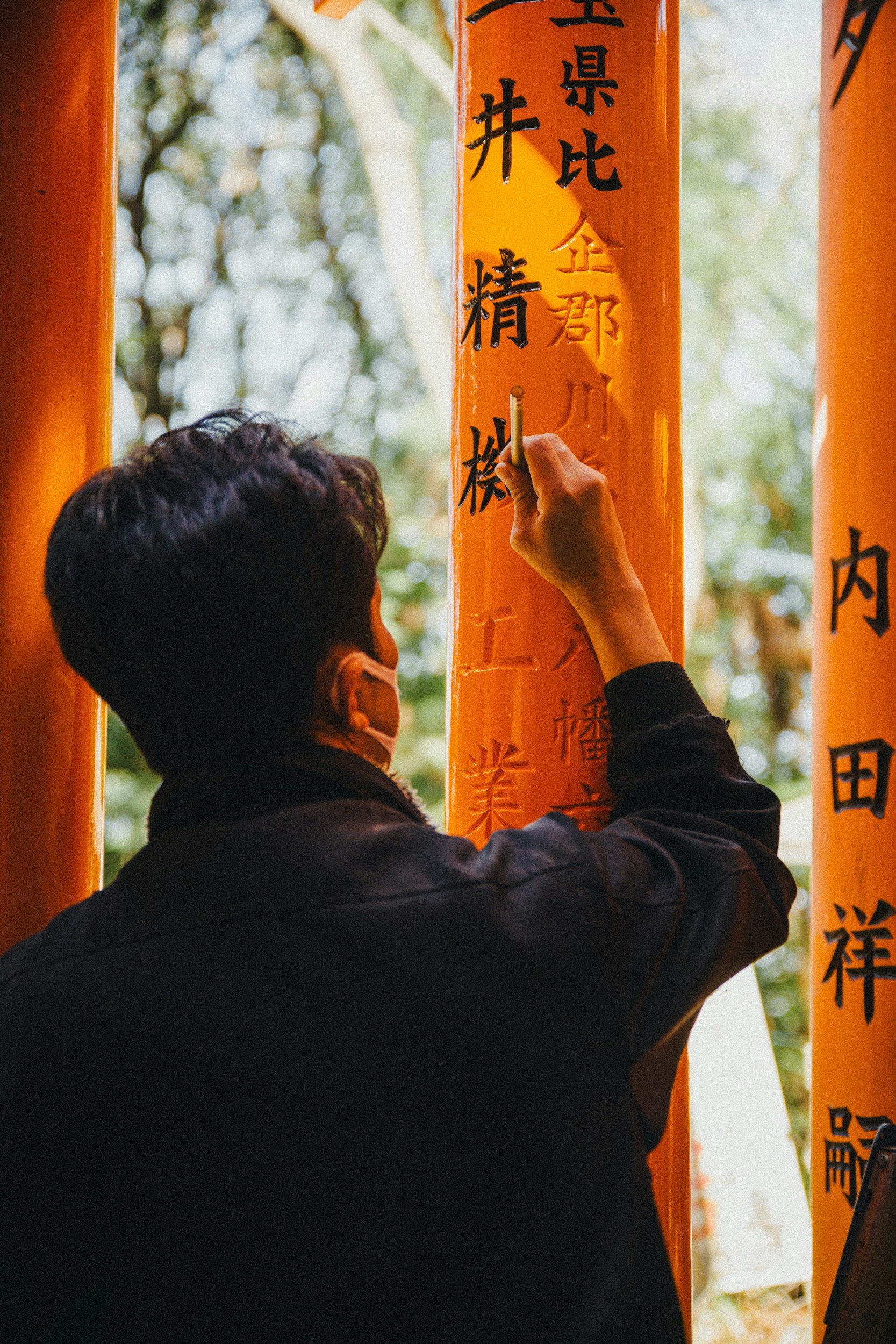 A man writes Japanese text on a wooden structure.