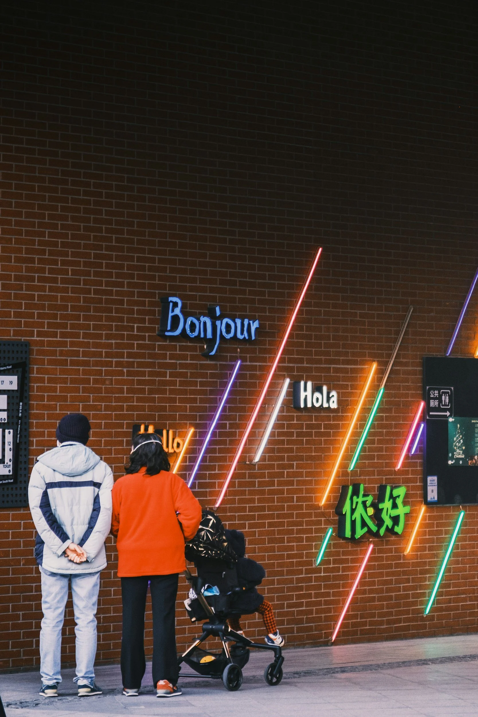 People look at neon signs with greetings in different languages.