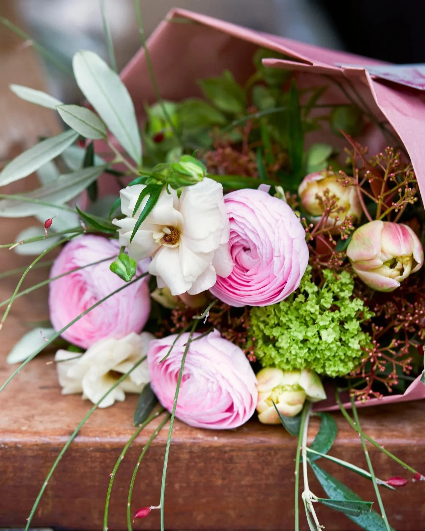 Blumenstrauß mit pinken und weißen Blumen, eingepackt in rosa Papier, auf einem Holztablett