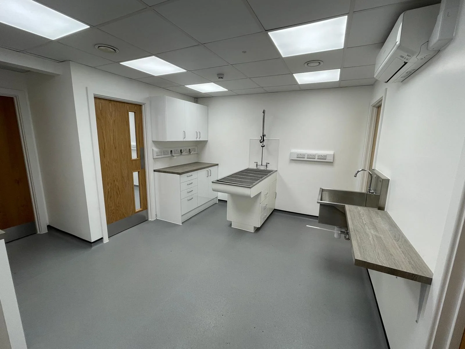 Empty hospital or laboratory room with white cabinets, a sink, and an examination or work station in a sterile environment.