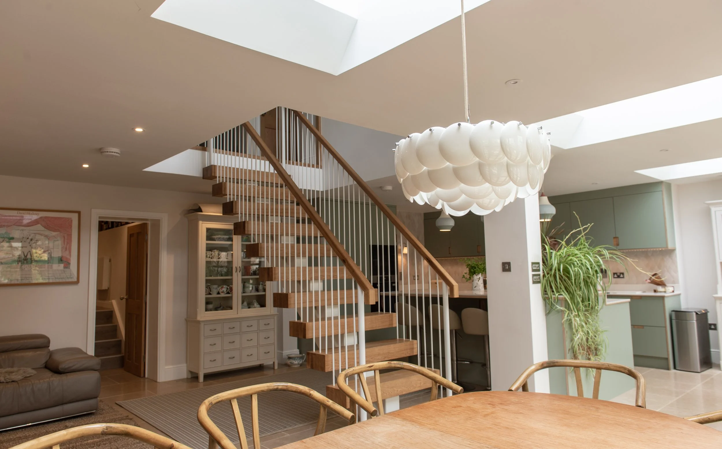 Interior view of a modern home with a staircase, hanging light fixture, and open kitchen area with plants.
