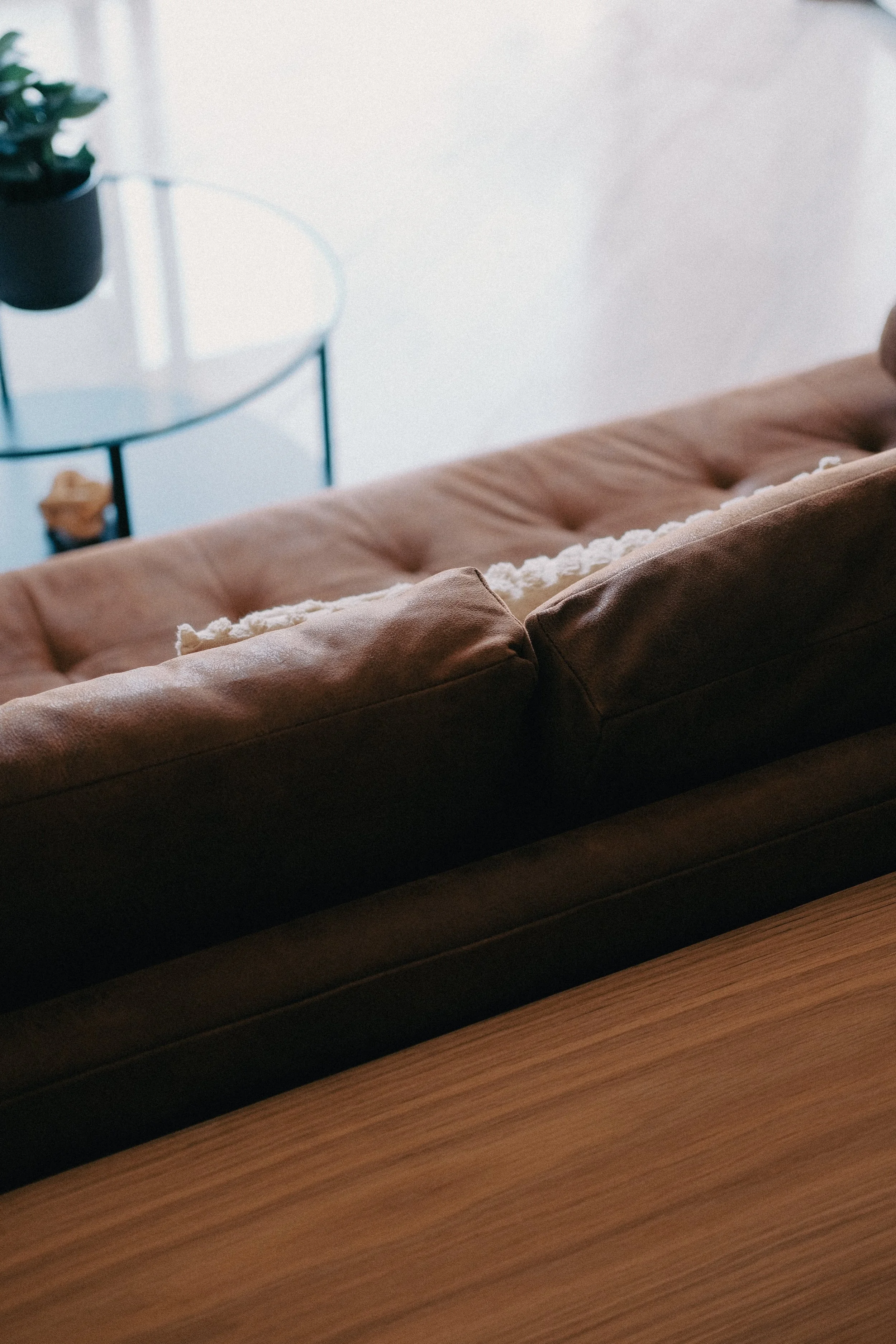 Brown leather couch with a rounded wooden table and a glass side table holding a small potted plant.