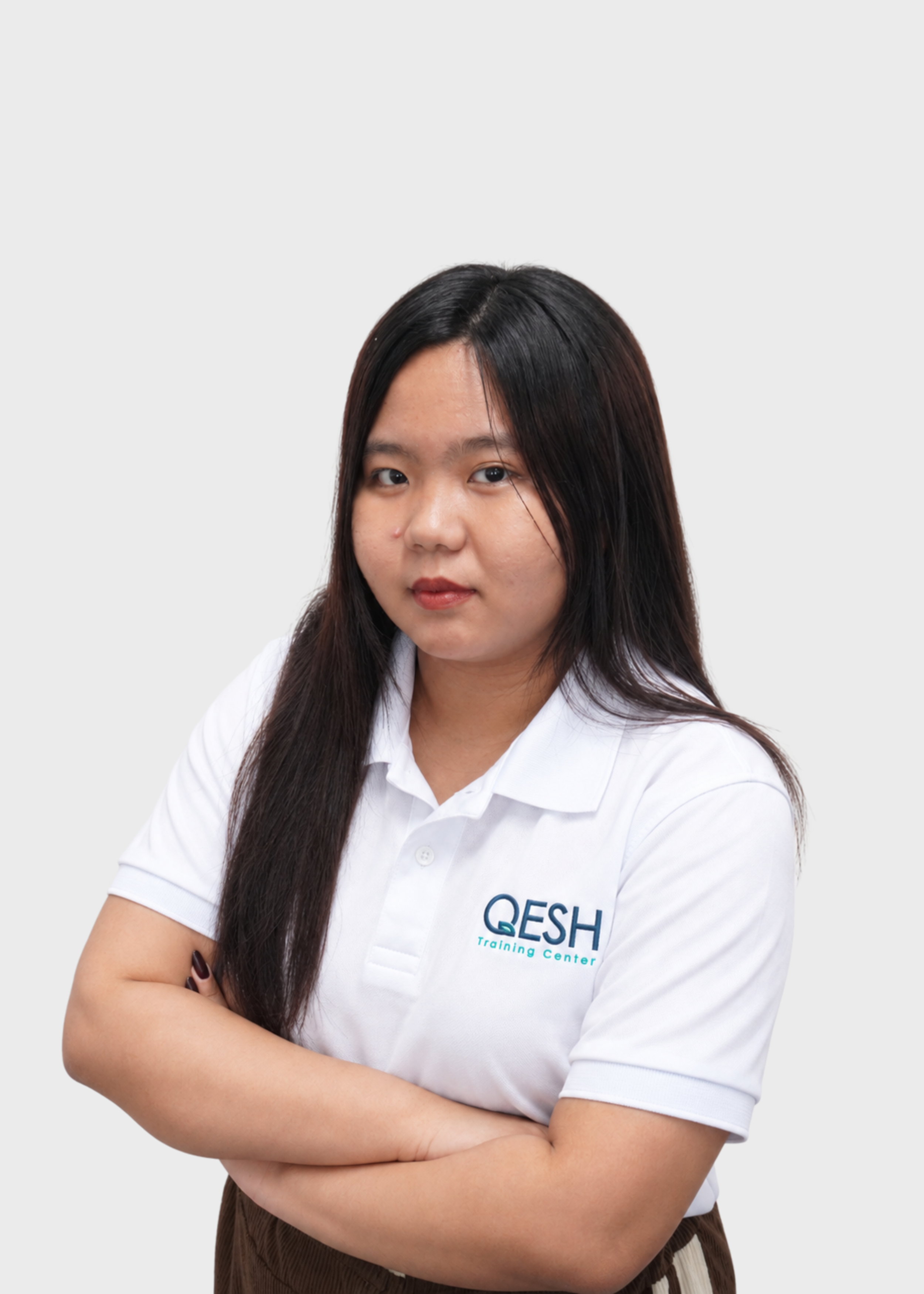 Person in a white shirt with folded arms and a name tag, wearing a "QESH Training Center" lanyard.