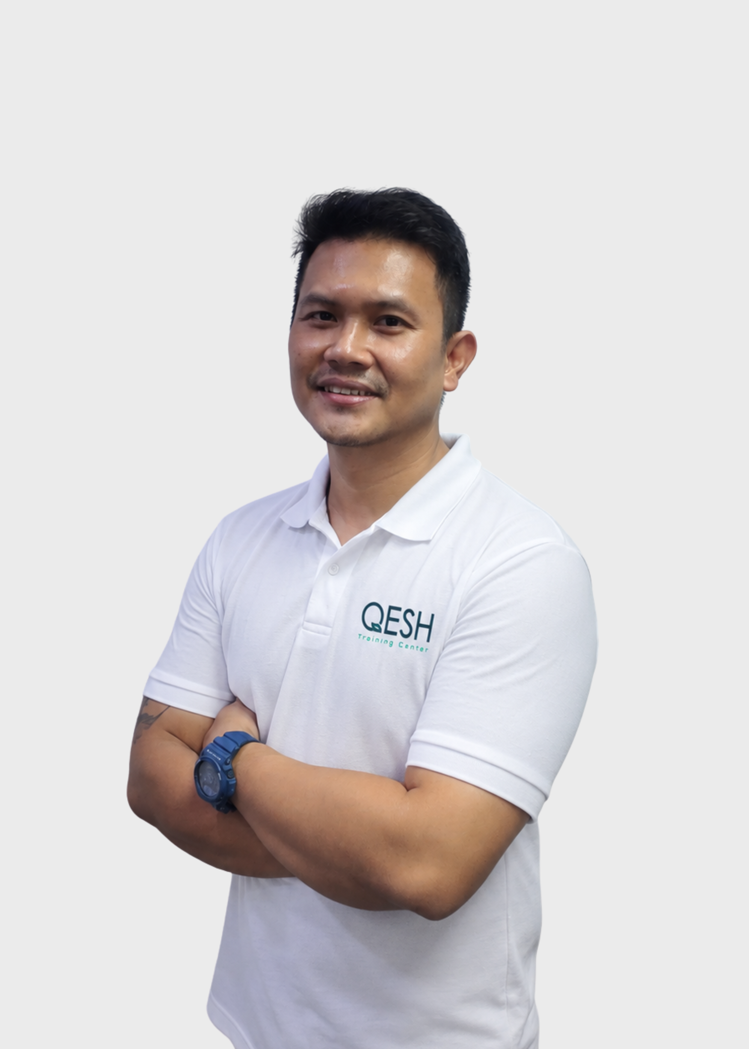 Man wearing a white and orange QESH branded polo, smiling with arms crossed and tattoo visible.