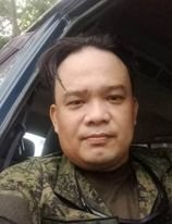 Person in camouflage uniform sitting in a vehicle, looking at the camera.