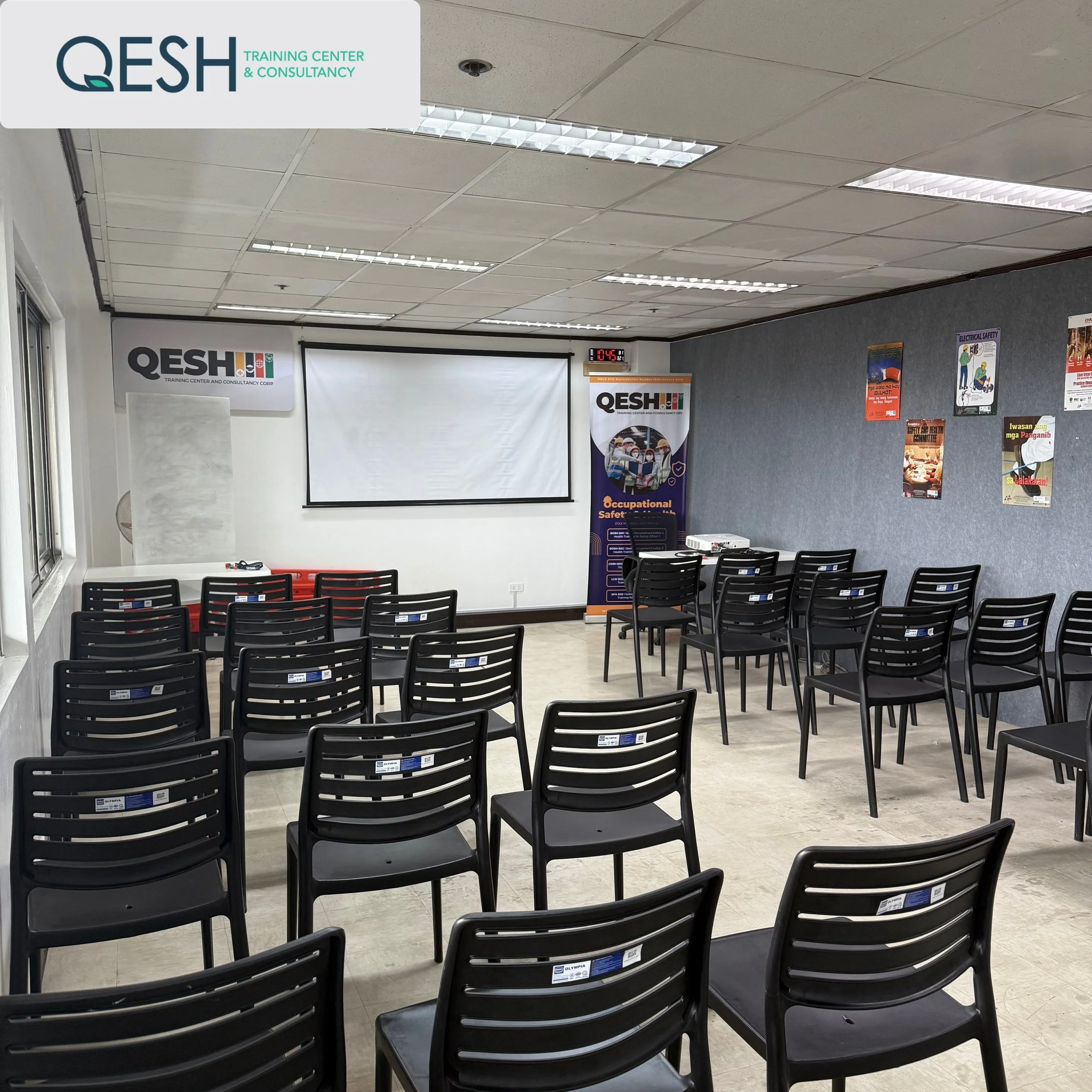 Empty training room with chairs facing a projector screen, posters on the wall, and a QESH Training Center and Consultancy logo visible.