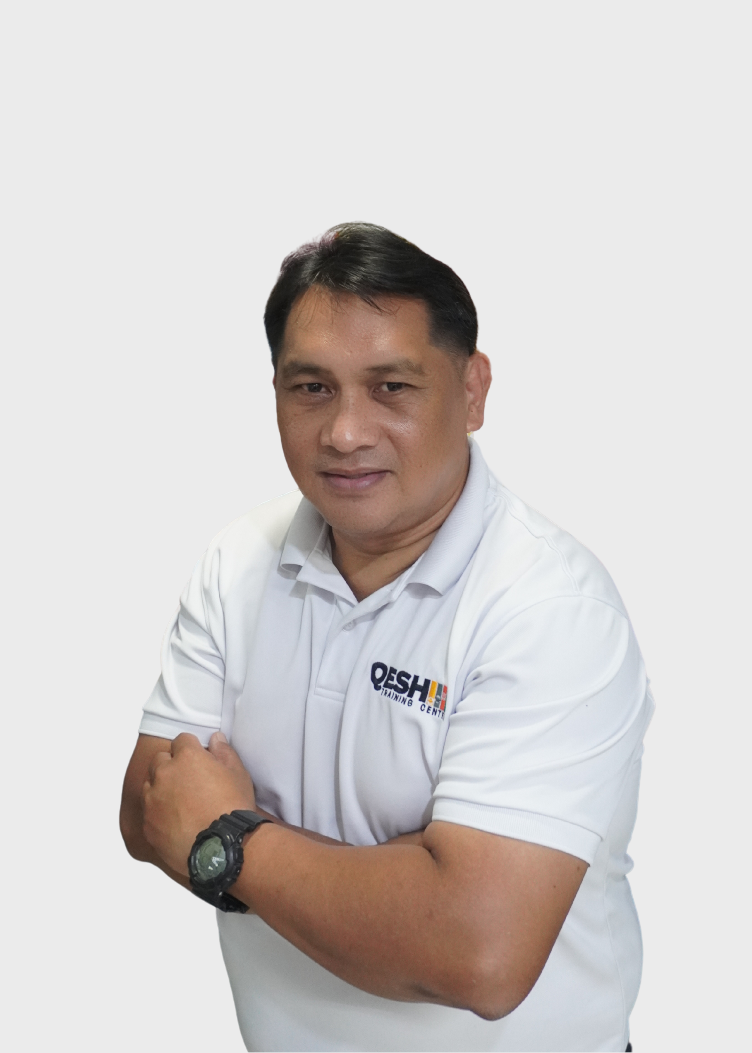 Man in a white QESH Training Center polo shirt with arms crossed, wearing a watch, against a neutral background.