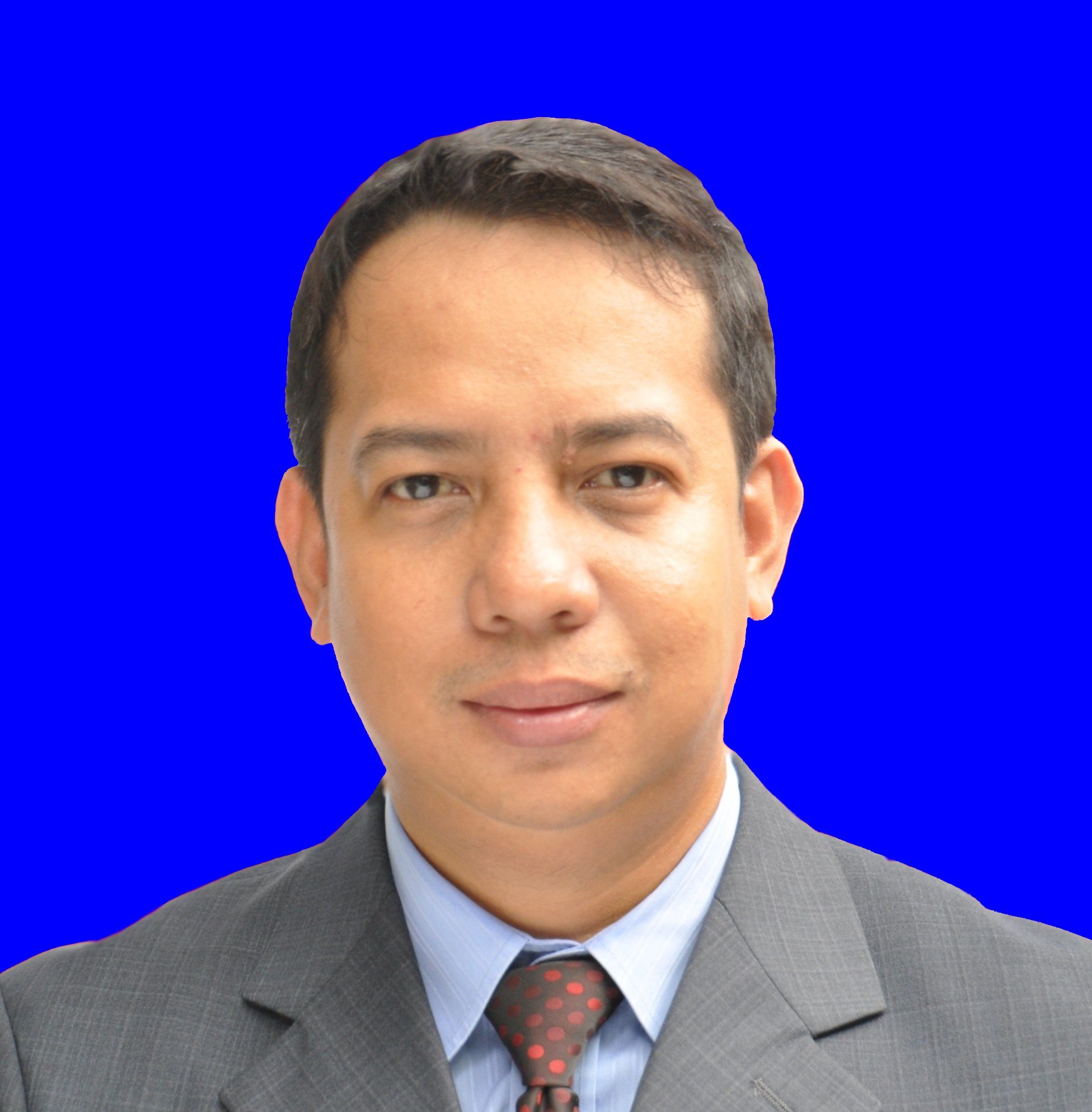 Man in a suit with a blue background, wearing a gray jacket, shirt, and polka dot tie.