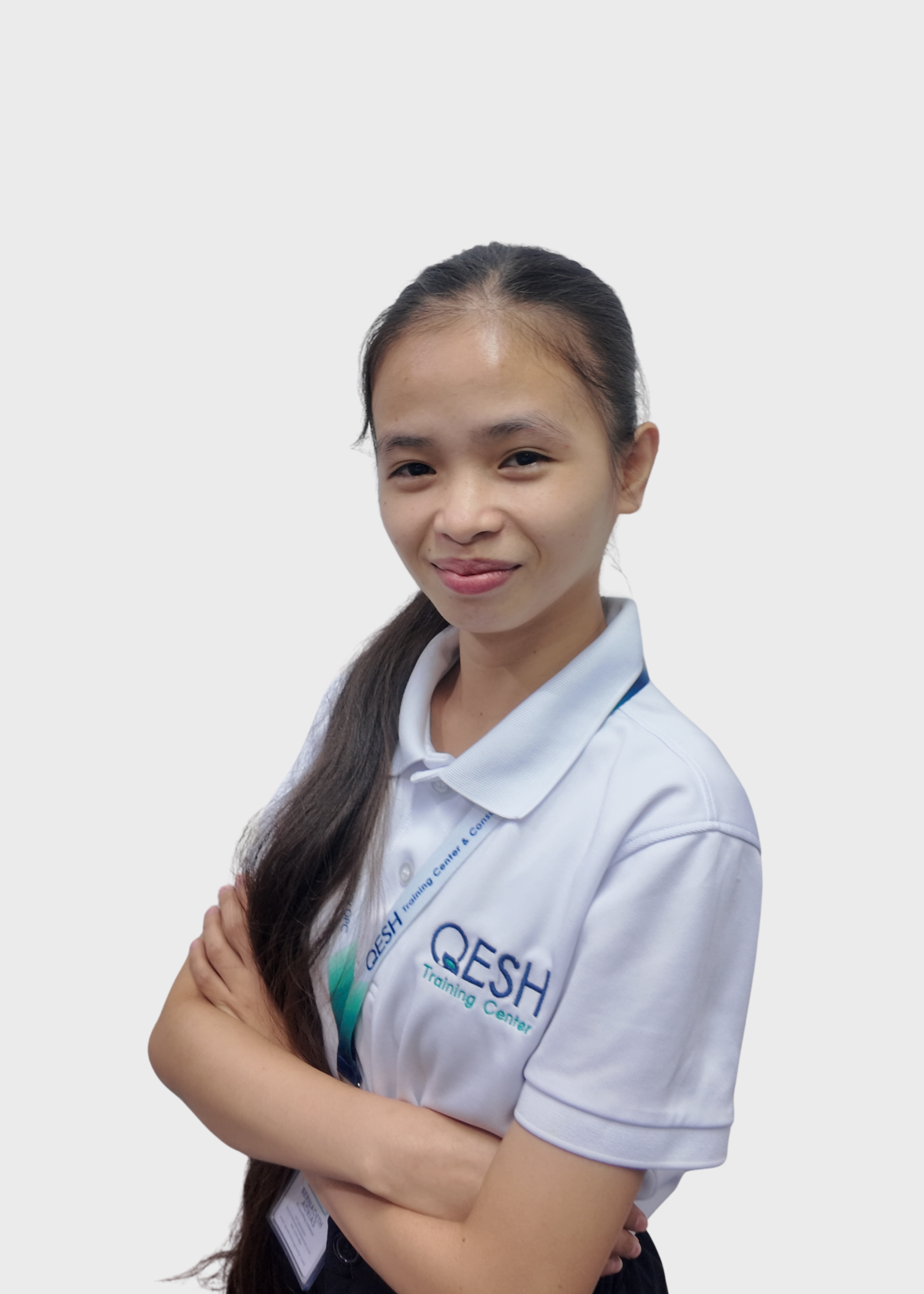 Person wearing a white polo shirt with "QESH" logo, crossed arms, smiling, and wearing a blue lanyard.