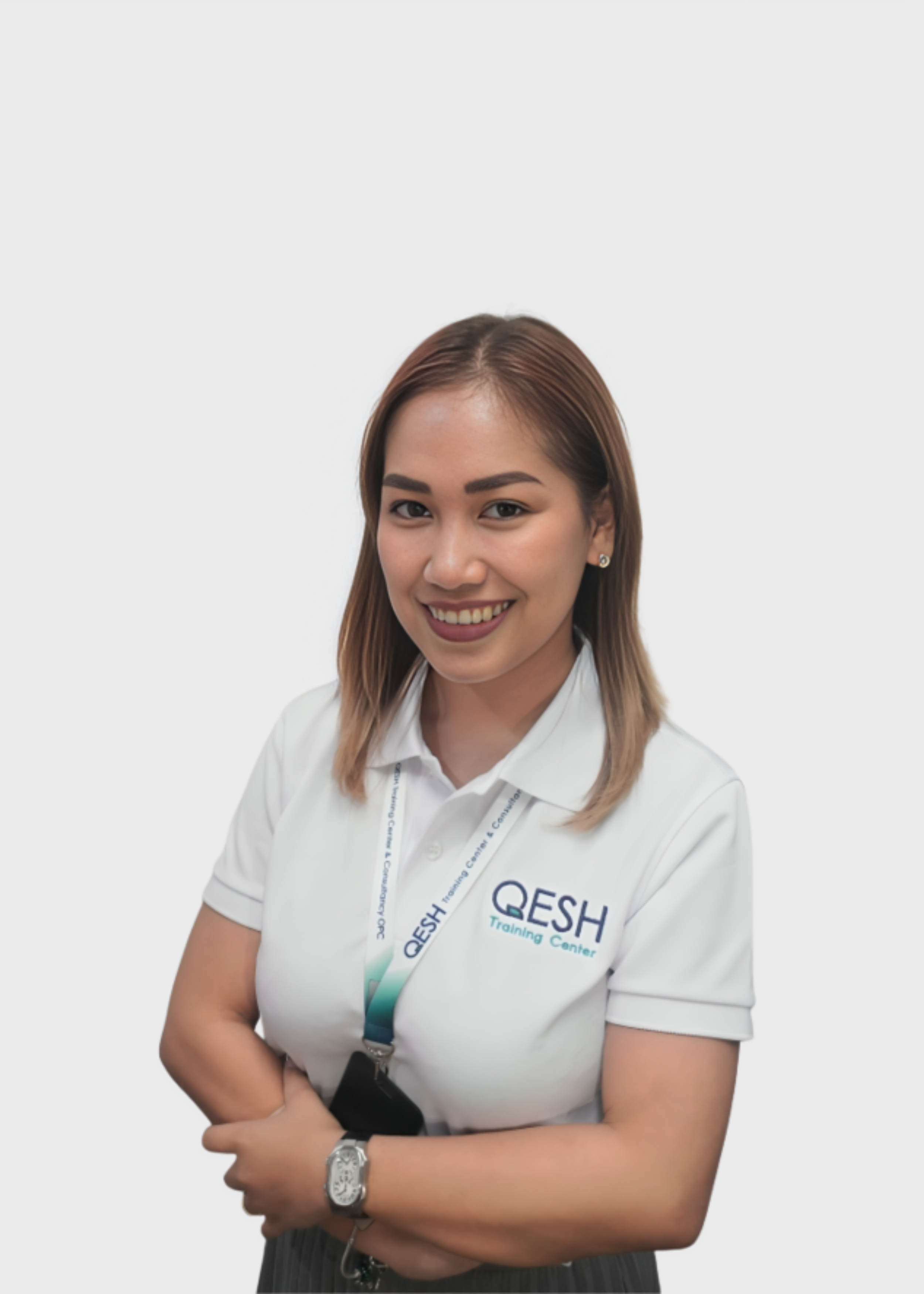 Person wearing a white polo shirt with 'QESH Training Center' logo, smiling with folded arms against a light gray background.