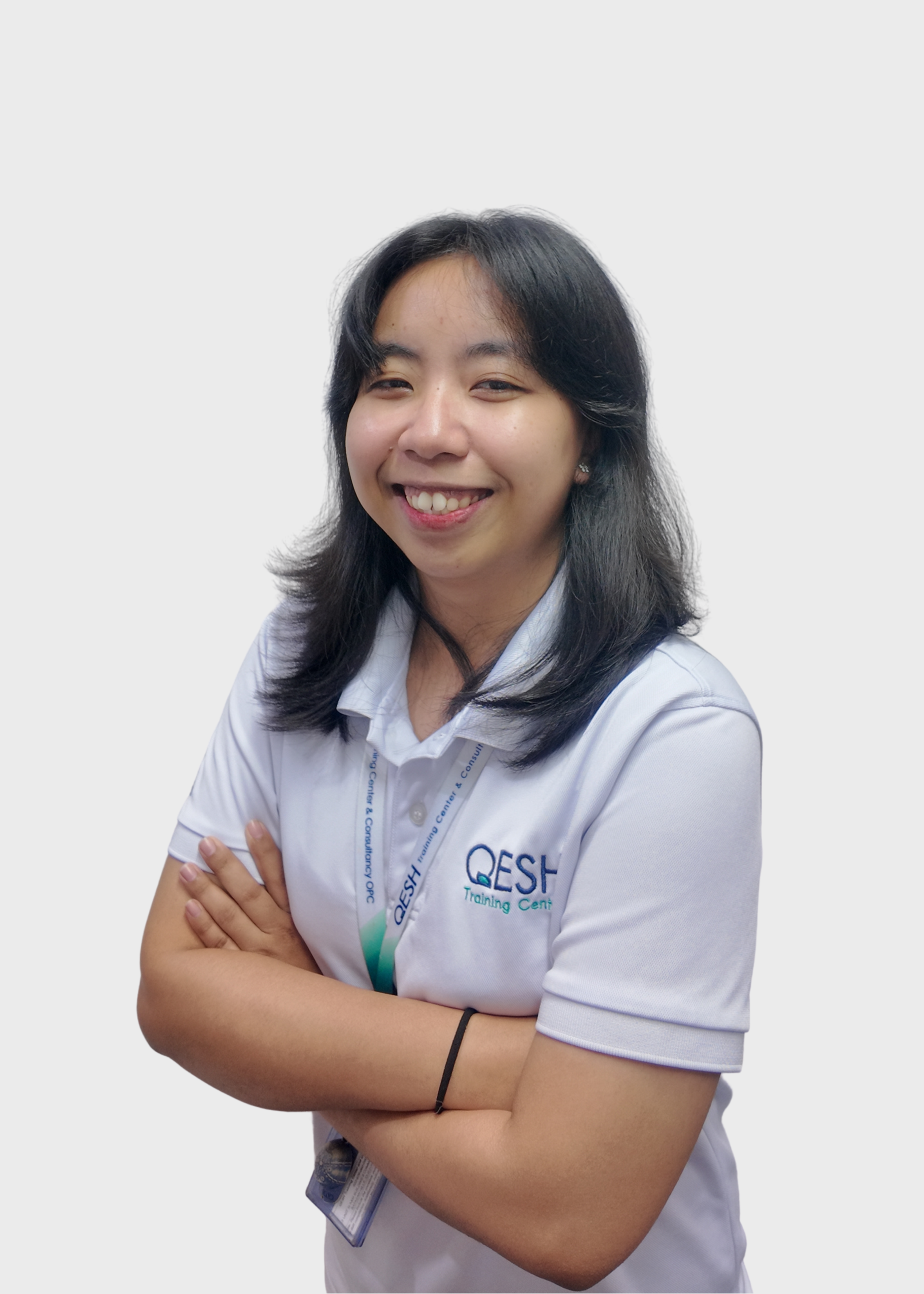 Person wearing a white QESH Training Center polo shirt, glasses, and a lanyard, posing with arms crossed.