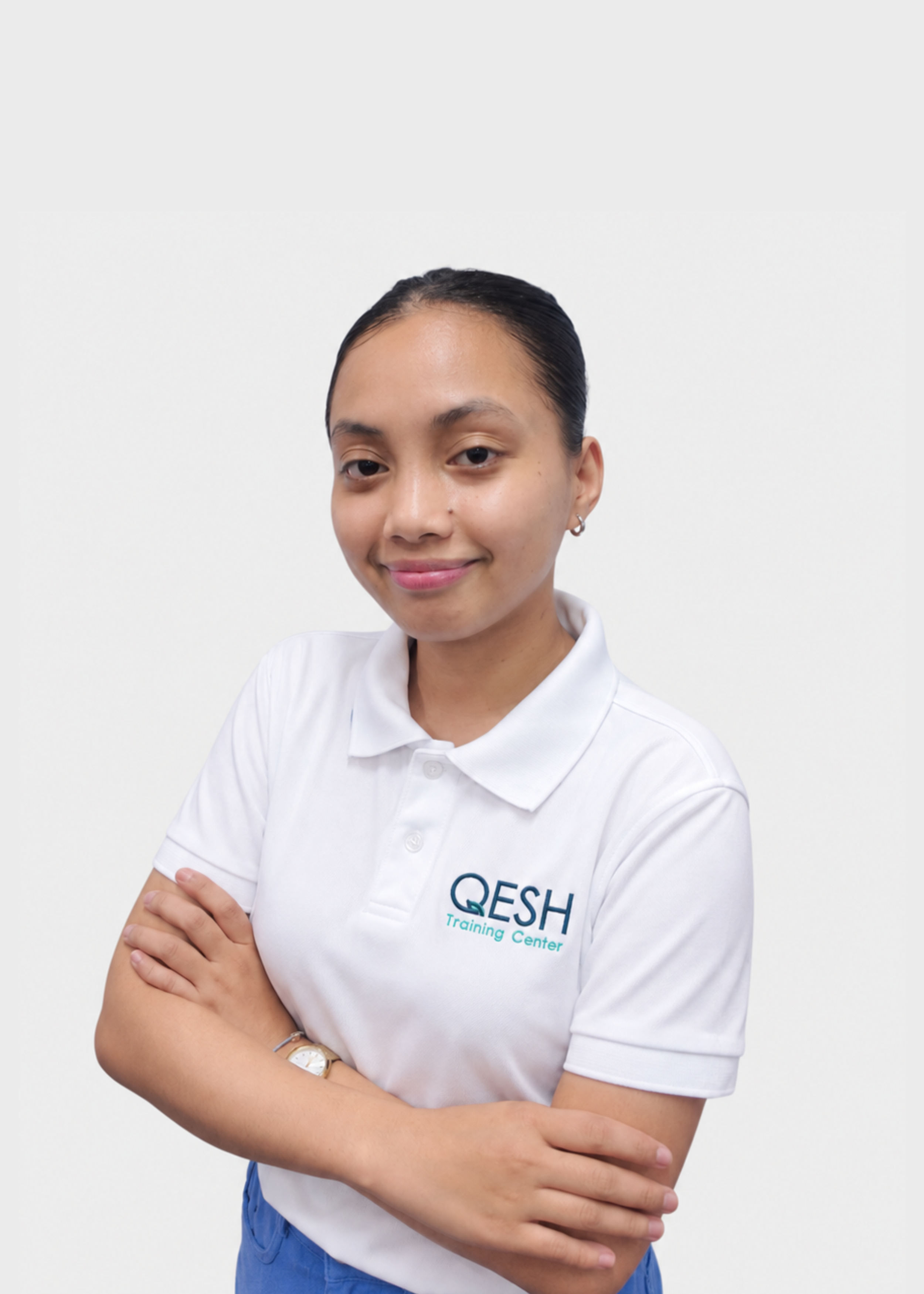 Person wearing a white polo shirt with "OESHI Training Center" logo and a lanyard, smiling, arms crossed.