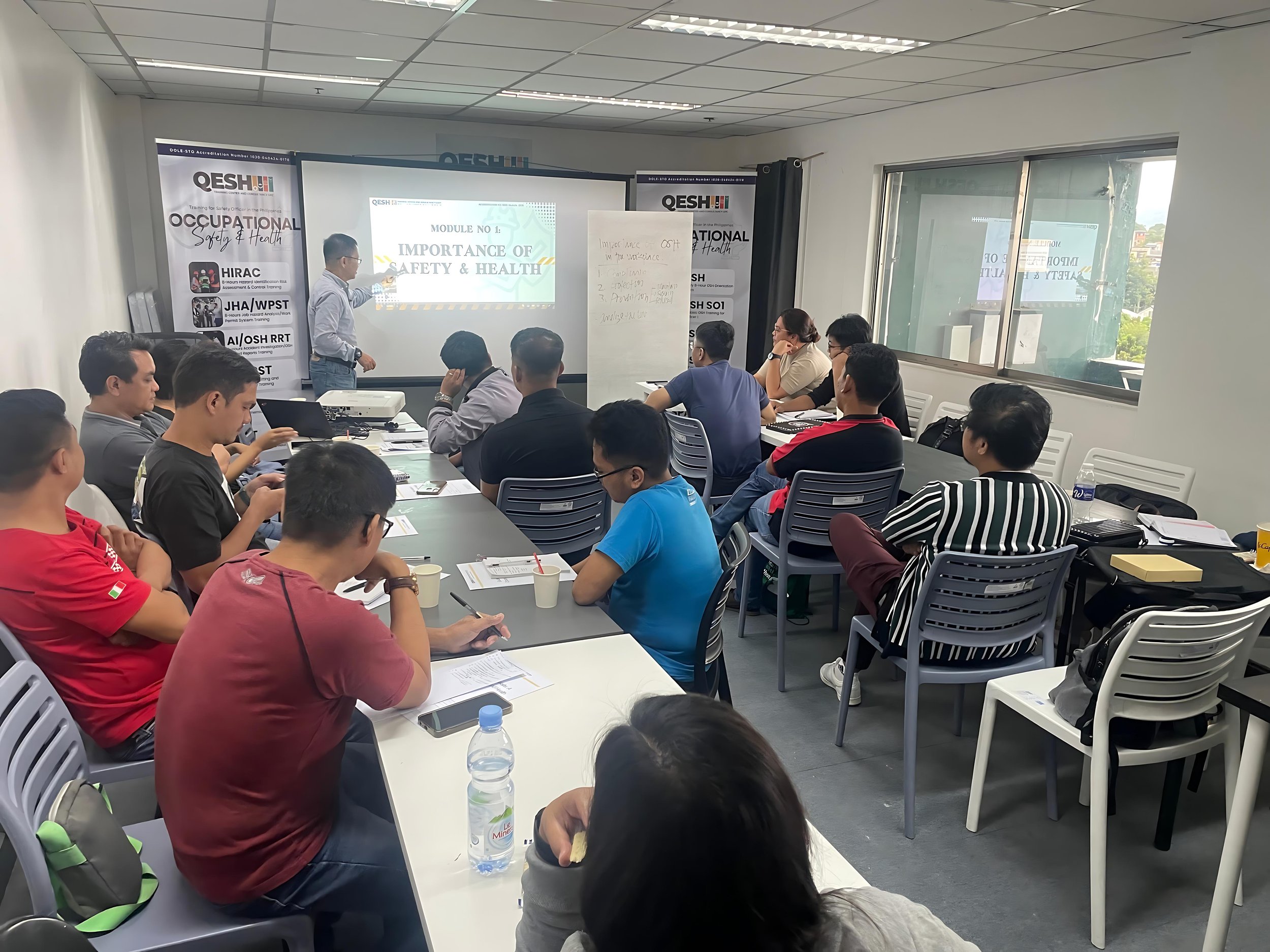 A group of people attending a safety and health training session in a classroom, with a presentation on the importance of safety and health being projected on a screen.