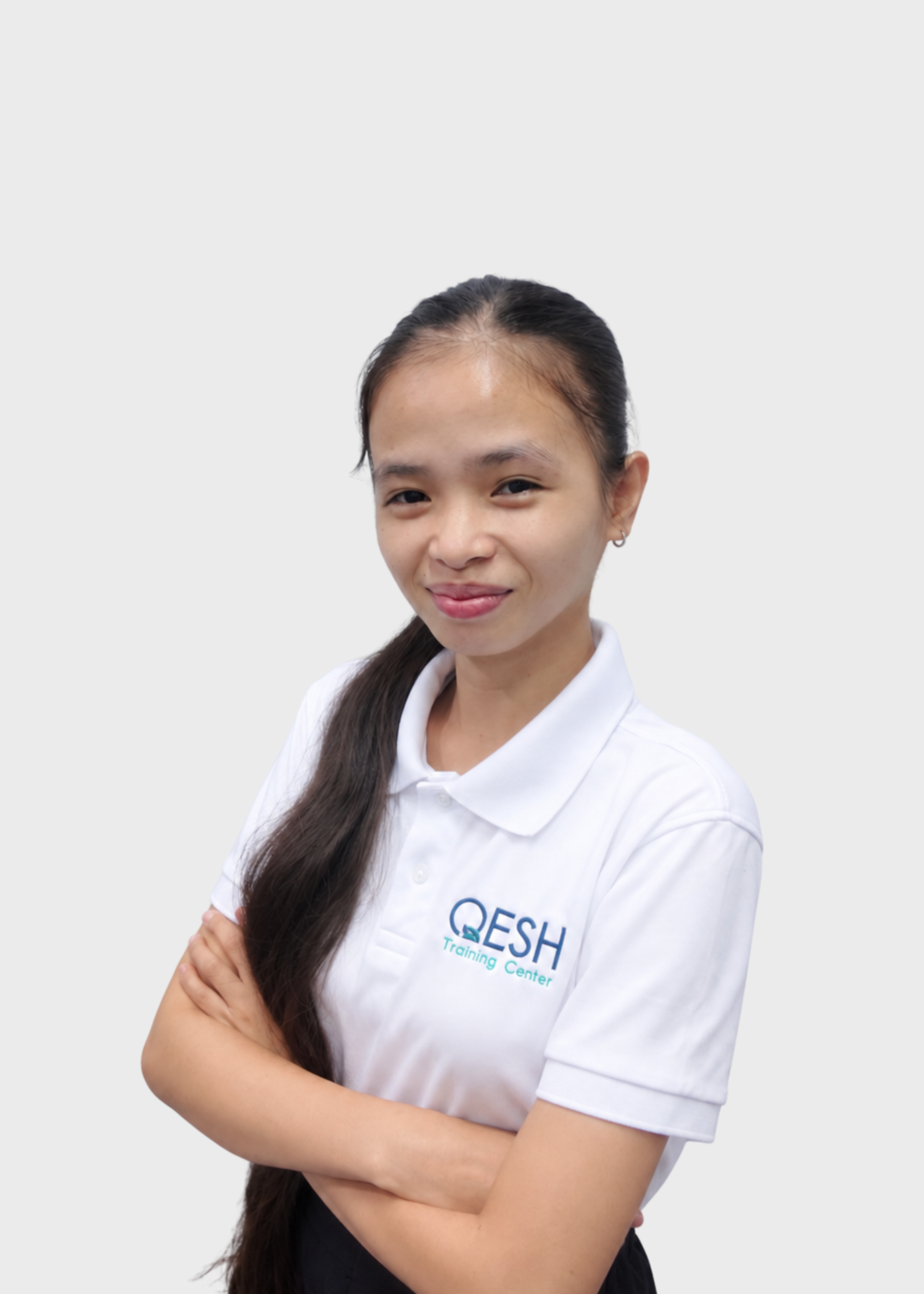 Person wearing a white polo shirt with "QESH" logo, crossed arms, smiling, and wearing a blue lanyard.