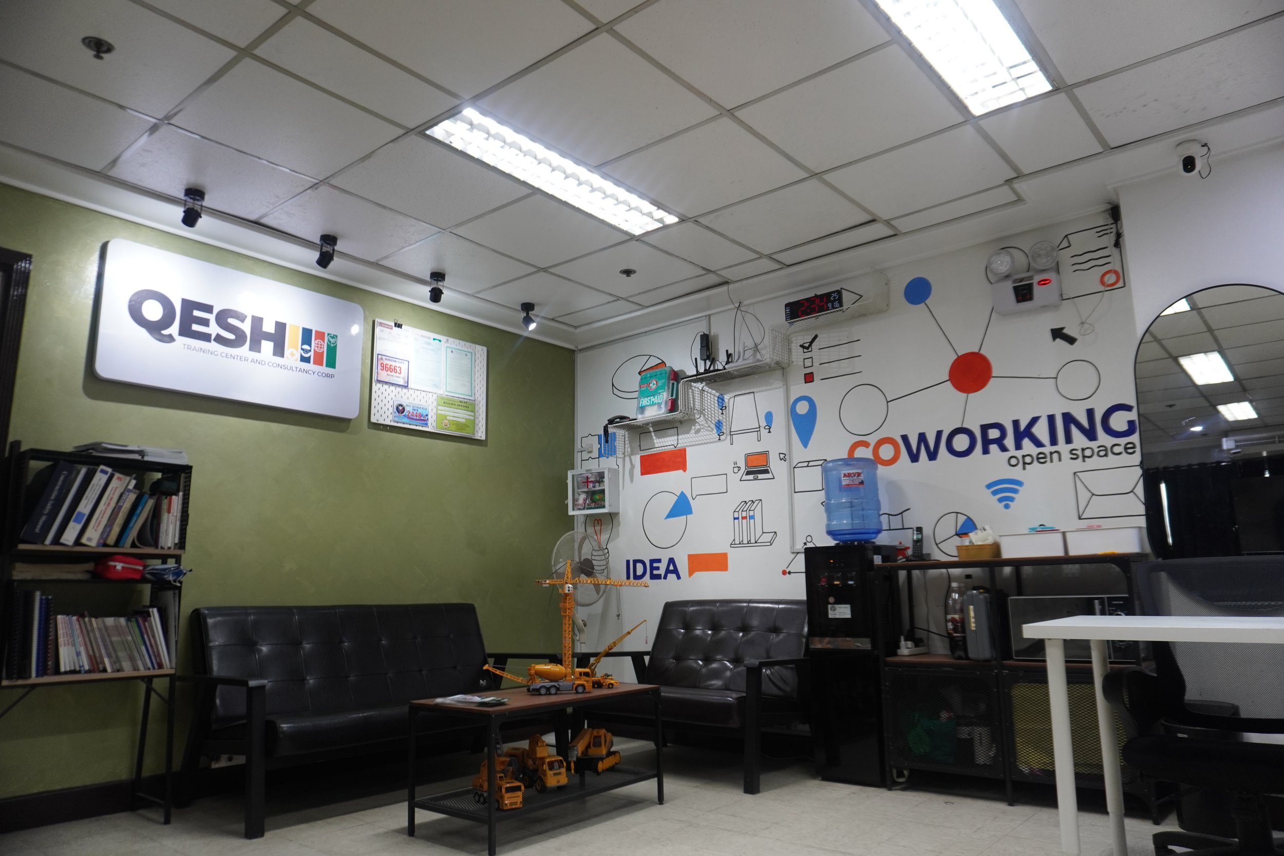 Coworking space interior with sofas, wall art, bookshelves, and a water cooler.