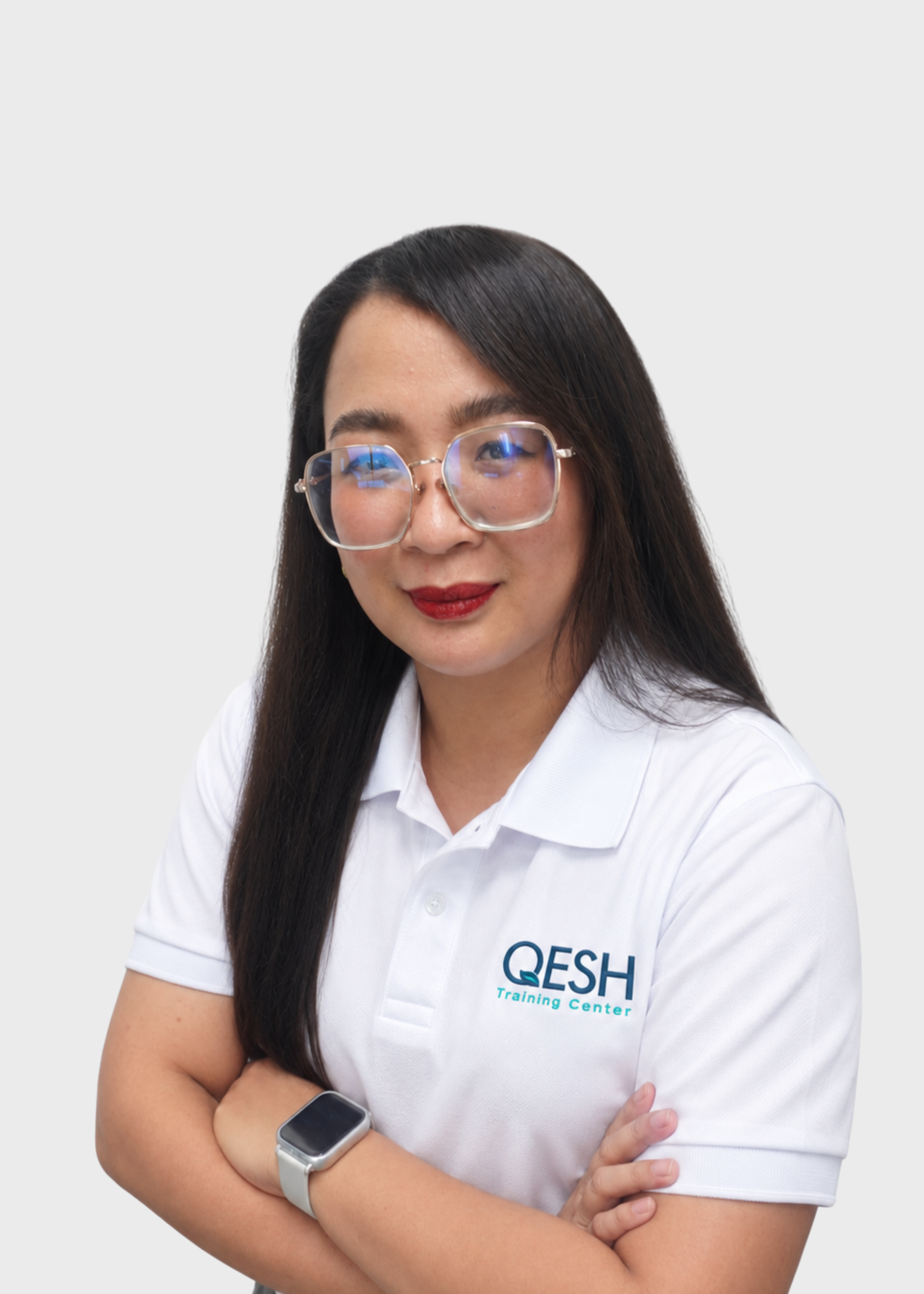 Person with long straight hair, wearing glasses and a white polo shirt with "QESH Training" logo, arms crossed.