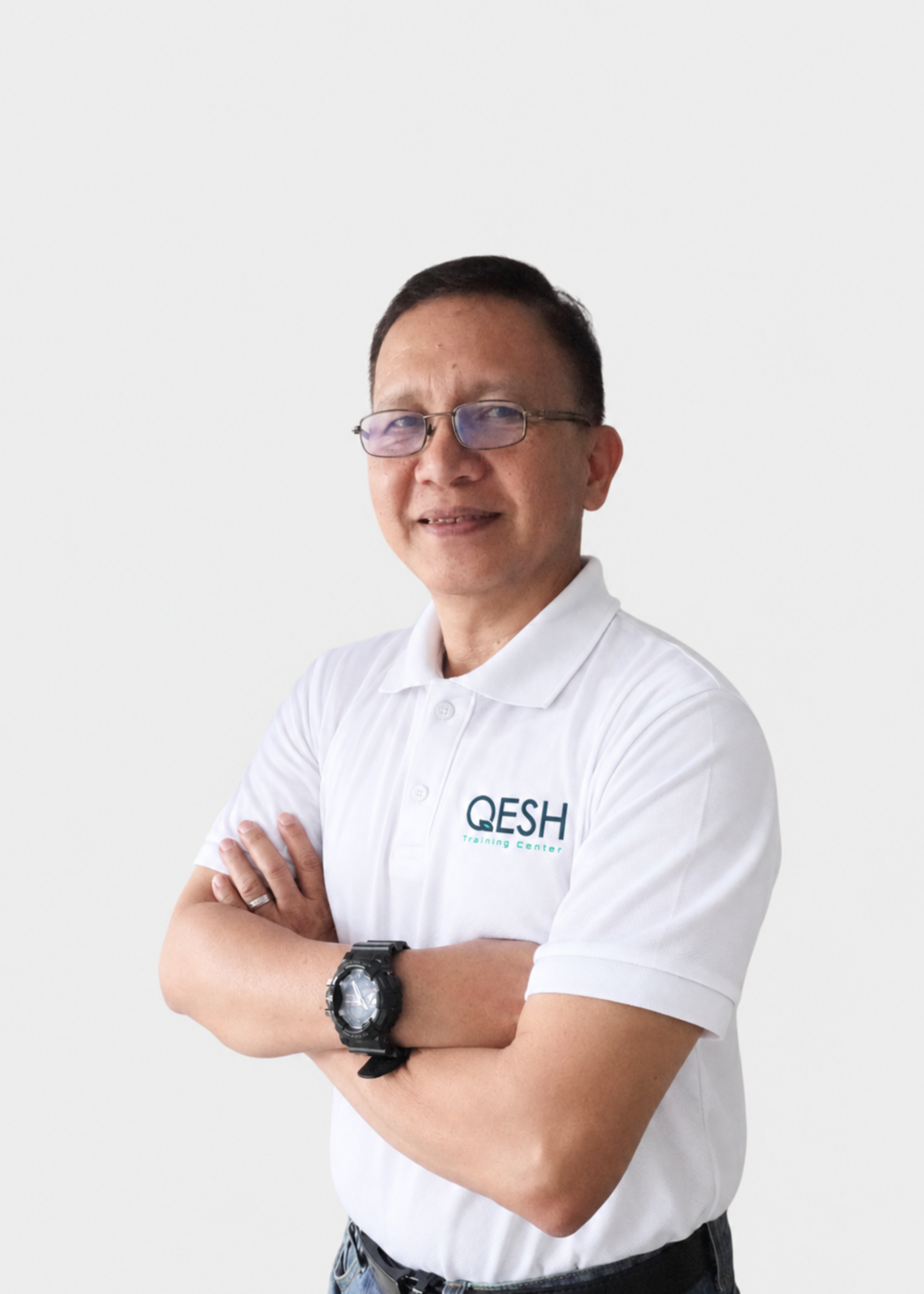 Man wearing a multi-colored polo shirt with "QESH TRAINING" logo, glasses, and a watch, standing with arms crossed against a plain background.