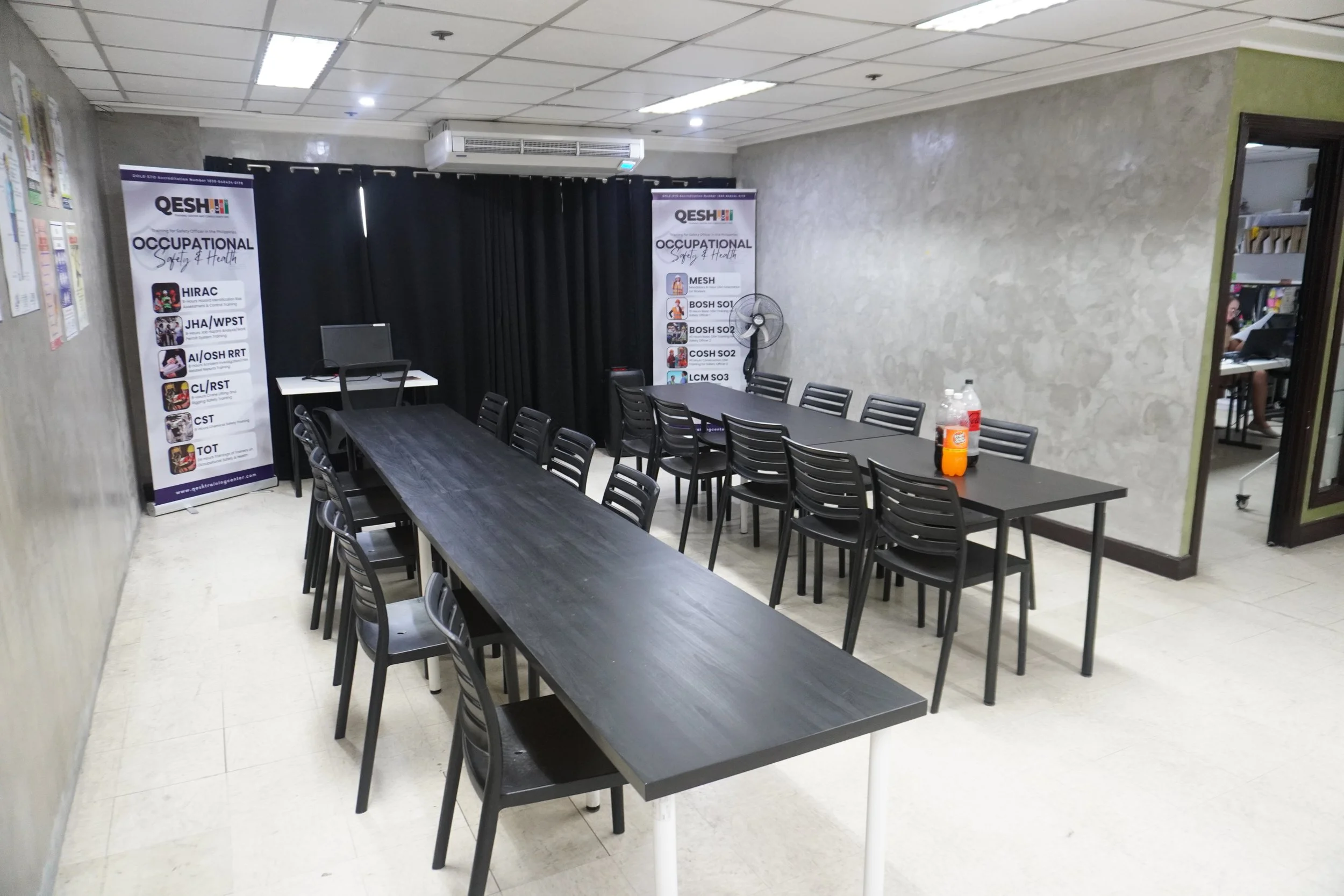 Conference room with long tables, chairs, banners, and training materials, featuring a laptop and soft drinks on the table.