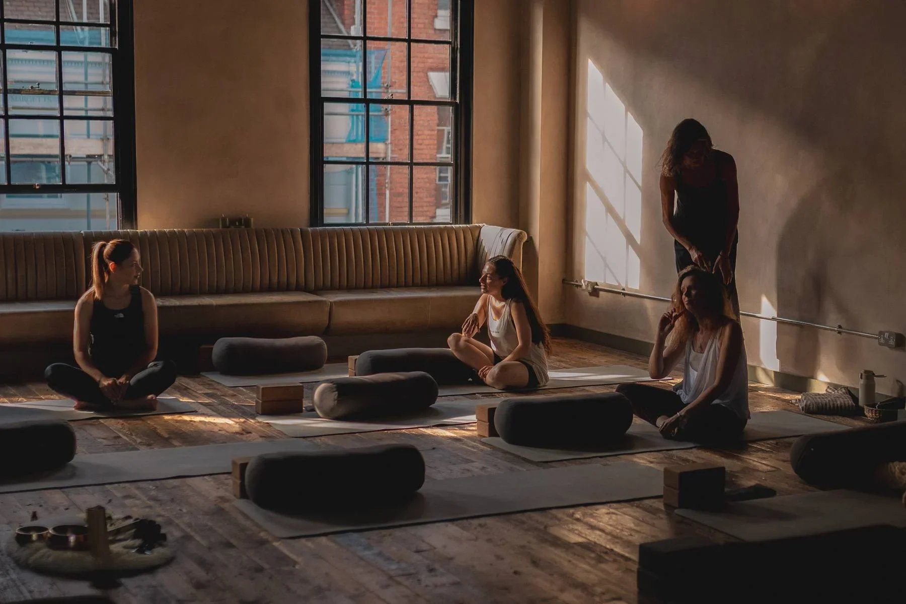 Yoga class at Heist House Studios Warwick — teacher offering hands-on adjustment as students sit on mats in warm morning light