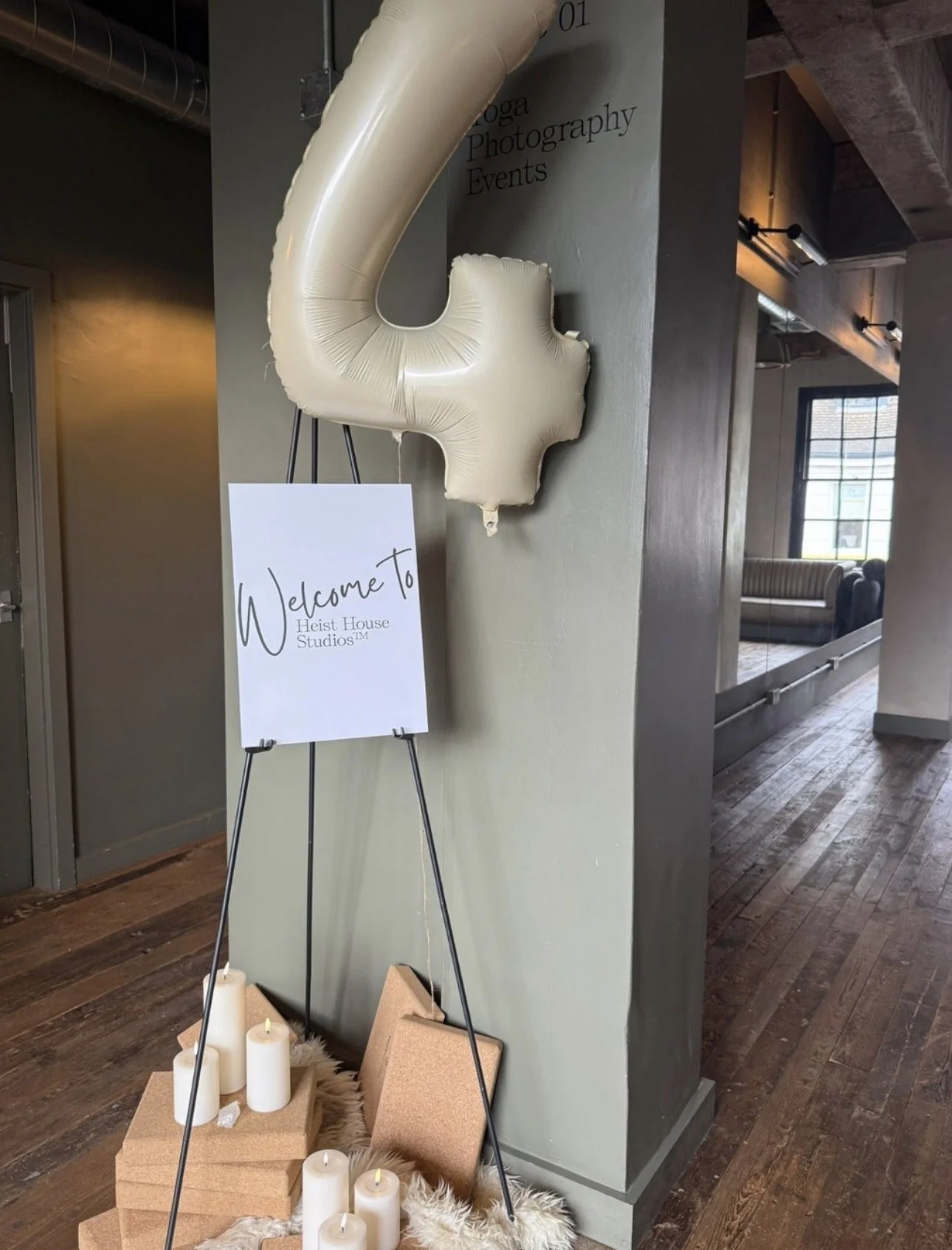 Welcome to Heist House Studios sign on an easel with a cream number 4 balloon, candles and yoga blocks — studio anniversary display in Warwick