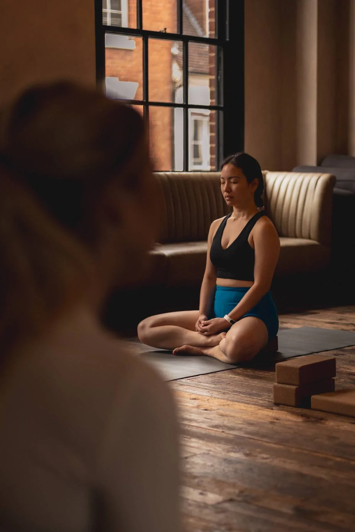 Woman seated in meditation during a restorative yoga class at Heist House Studios in Warwick, with yoga blocks on wooden studio floor.