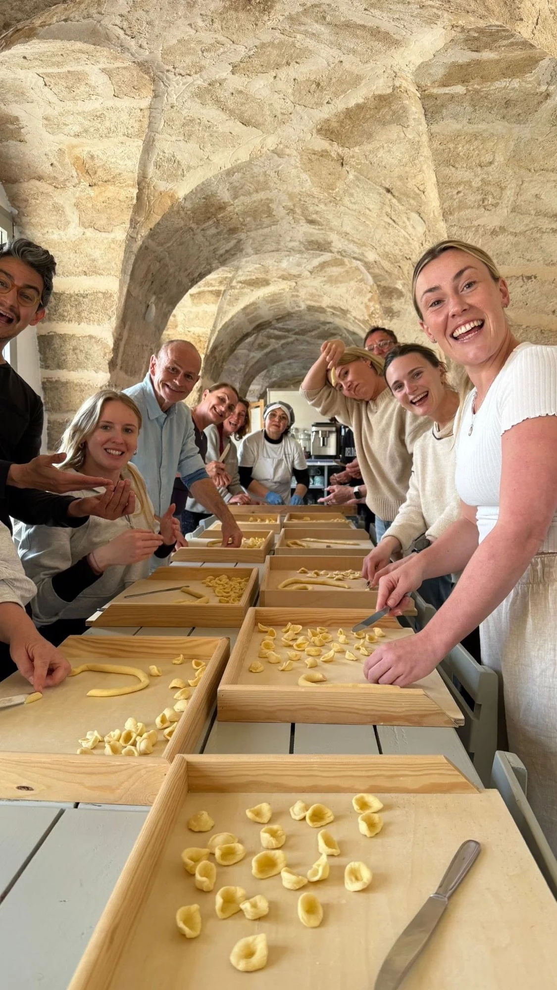 Retreat guests gathered around long wooden trays shaping orecchiette together during the pasta making class at Masseria Specula