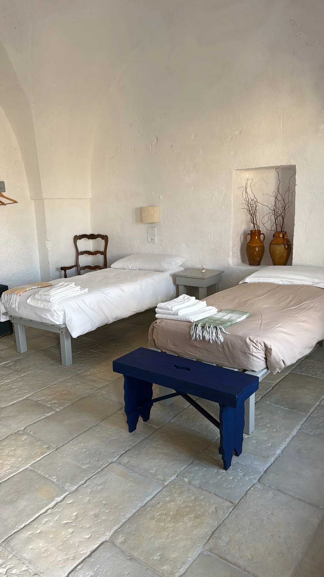 A simple whitewashed twin bedroom at Masseria Specula with a vaulted ceiling, stone floor and blue wooden bench