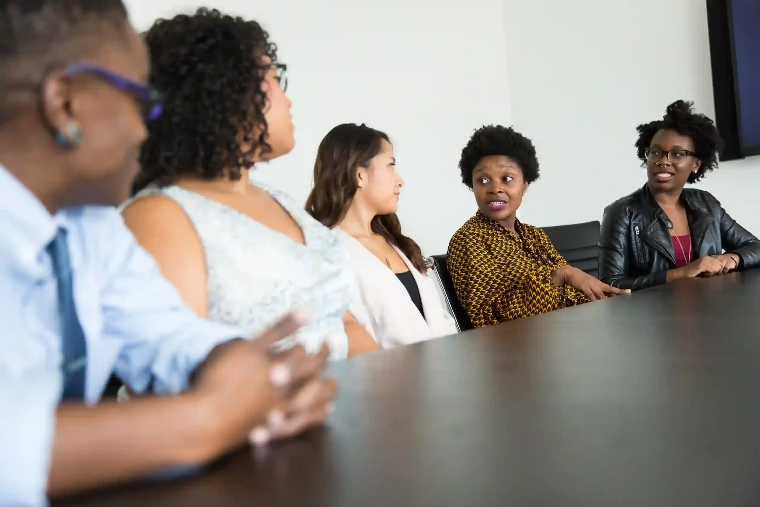 A diverse group of women sitting at a conference table engaged in a discussion.