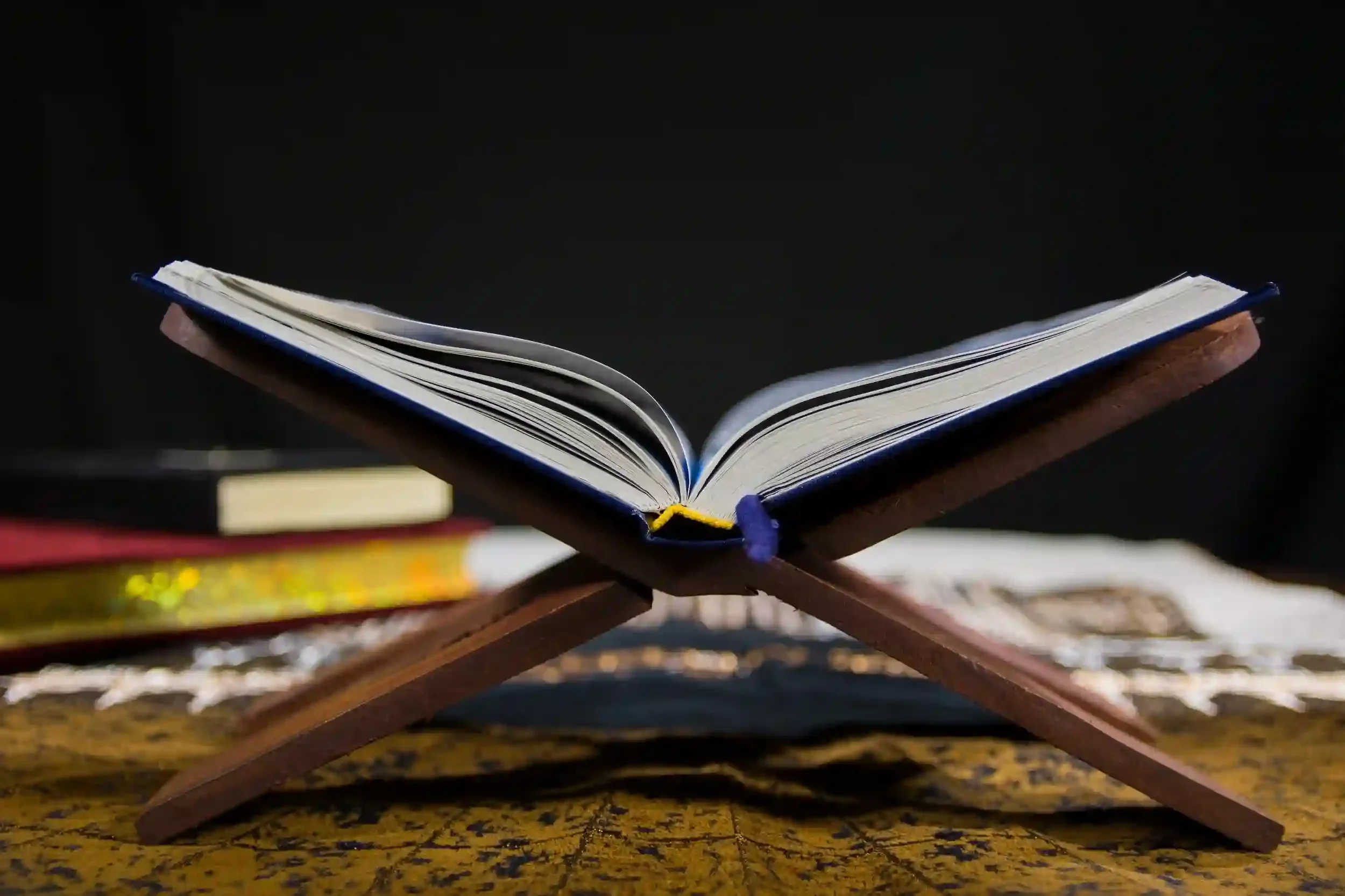 An open book rests on a wooden stand with a black background and appears to be illuminated.