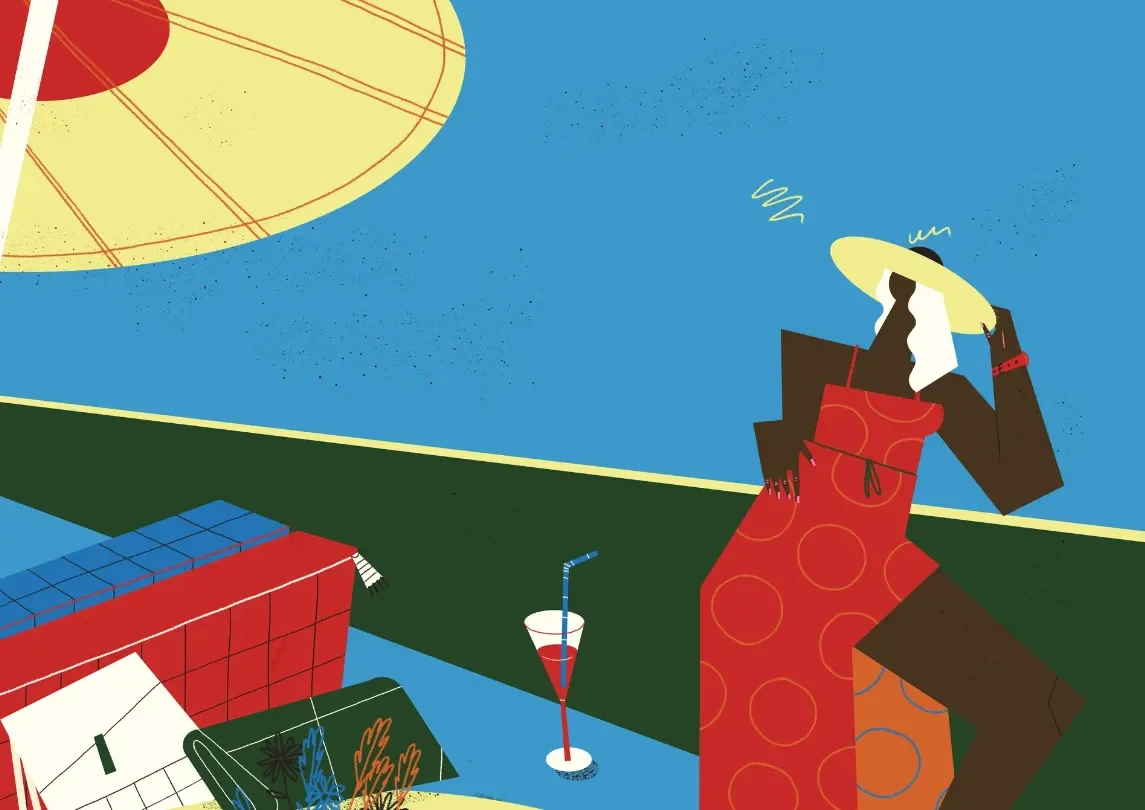 A woman in a red polka dot dress and yellow sunhat standing outdoors, with a drink and a book on a table nearby. The scene suggests a sunny day at a picnic or park.