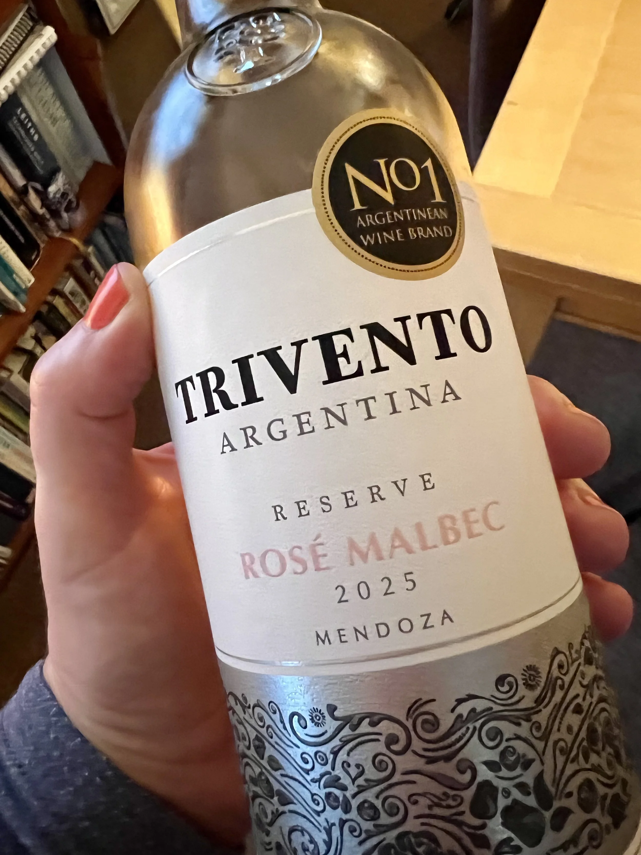 A hand holding a bottle of Trivento Reserve Rosé Malbec 2025 from Mendoza, Argentina, showing the white and silver label.