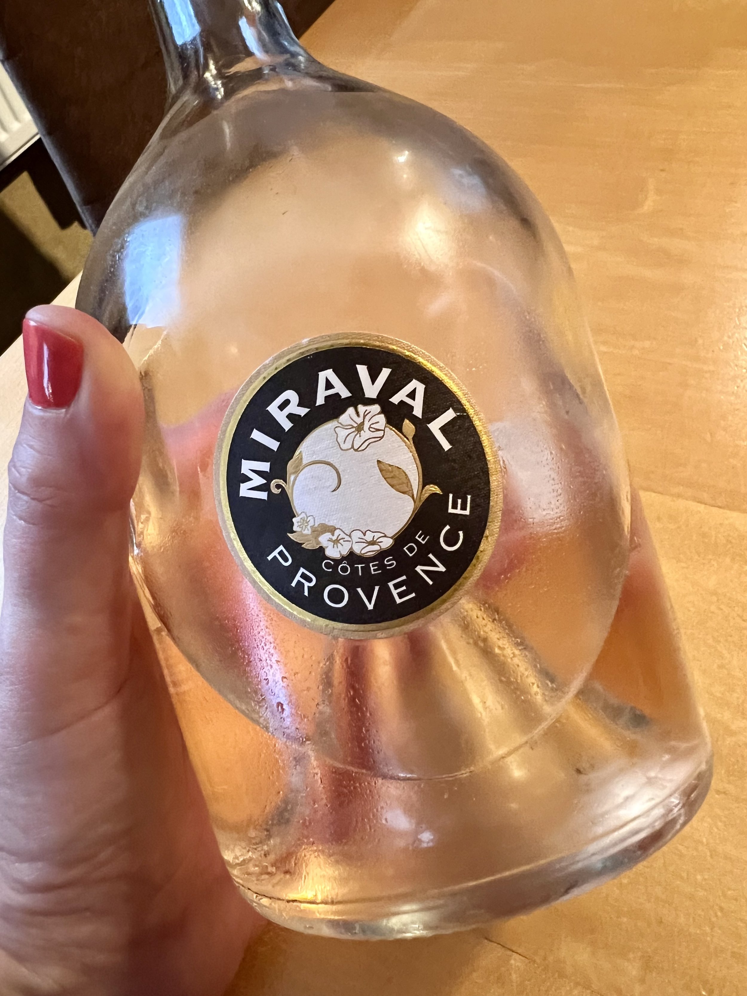 A hand holding the iconic, round-bottomed bottle of Miraval Côtes de Provence rosé wine with condensation on the glass.