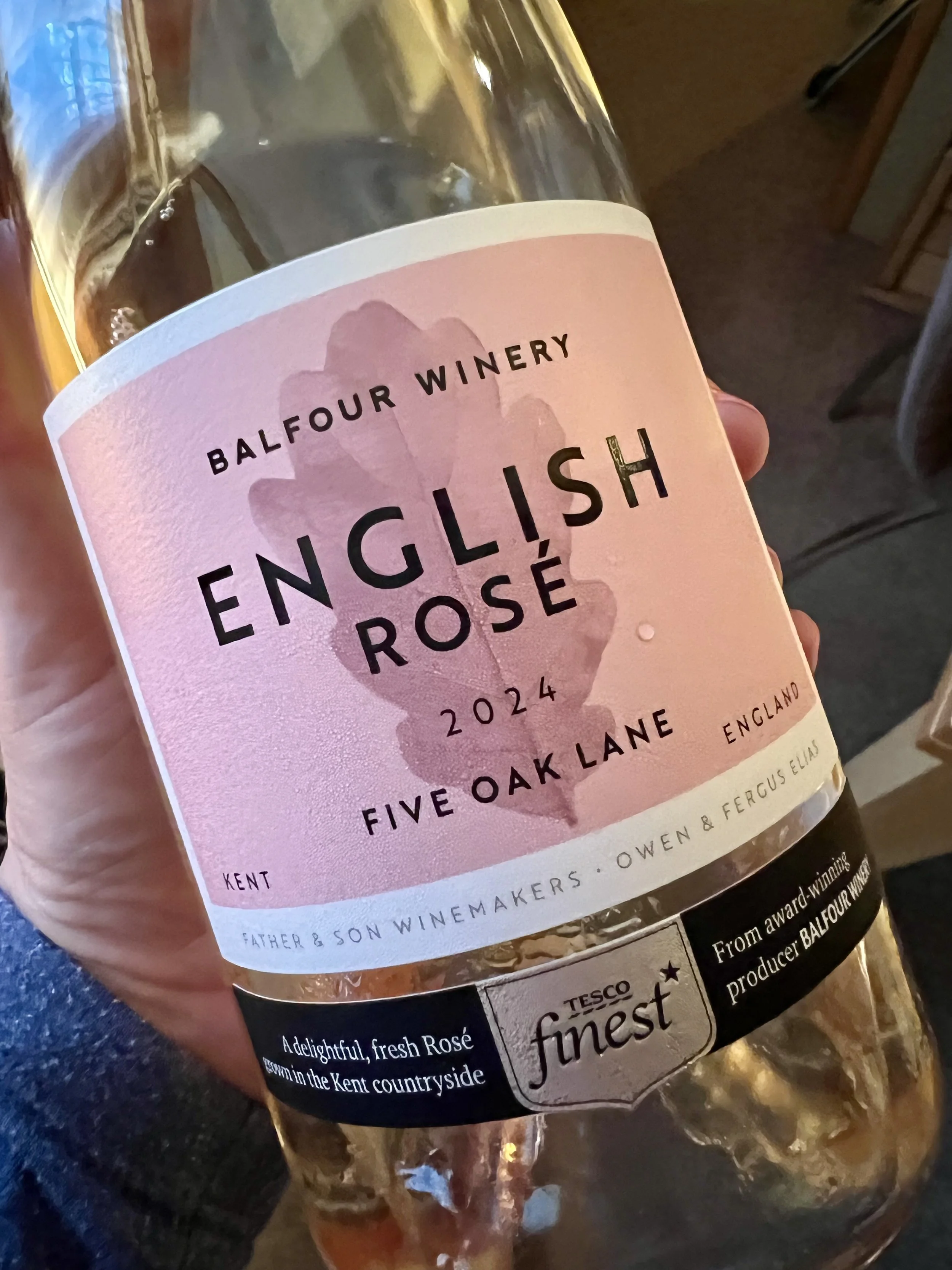 A close-up of a hand holding a bottle of Balfour Winery Five Oak Lane English Rosé 2024 from Kent, a Tesco Finest selection.
