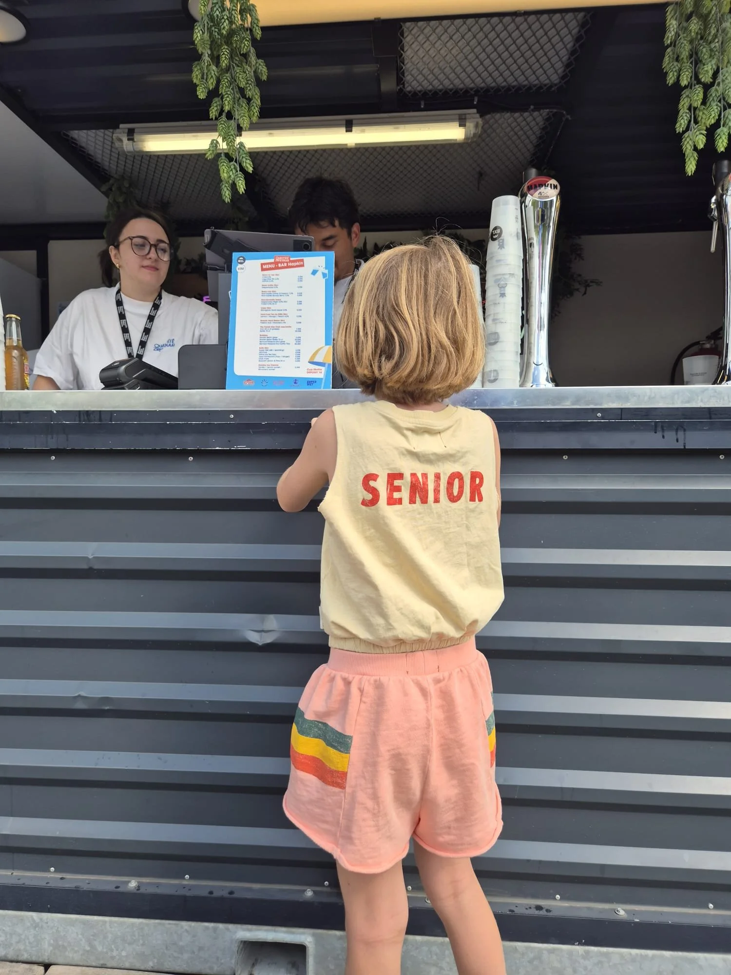 Little girl ordering drinks with a yellow tshirt saying "senior"