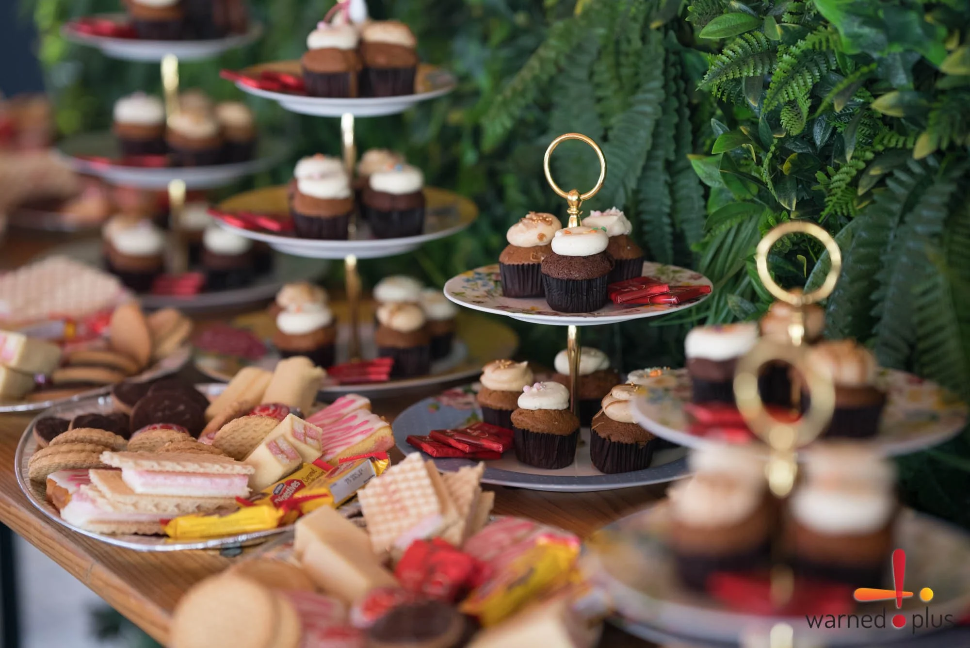 A table filled with colorful tiered dessert trays holding various sweets including cupcakes, cookies, chocolates, and wafers, arranged for a celebration or party.