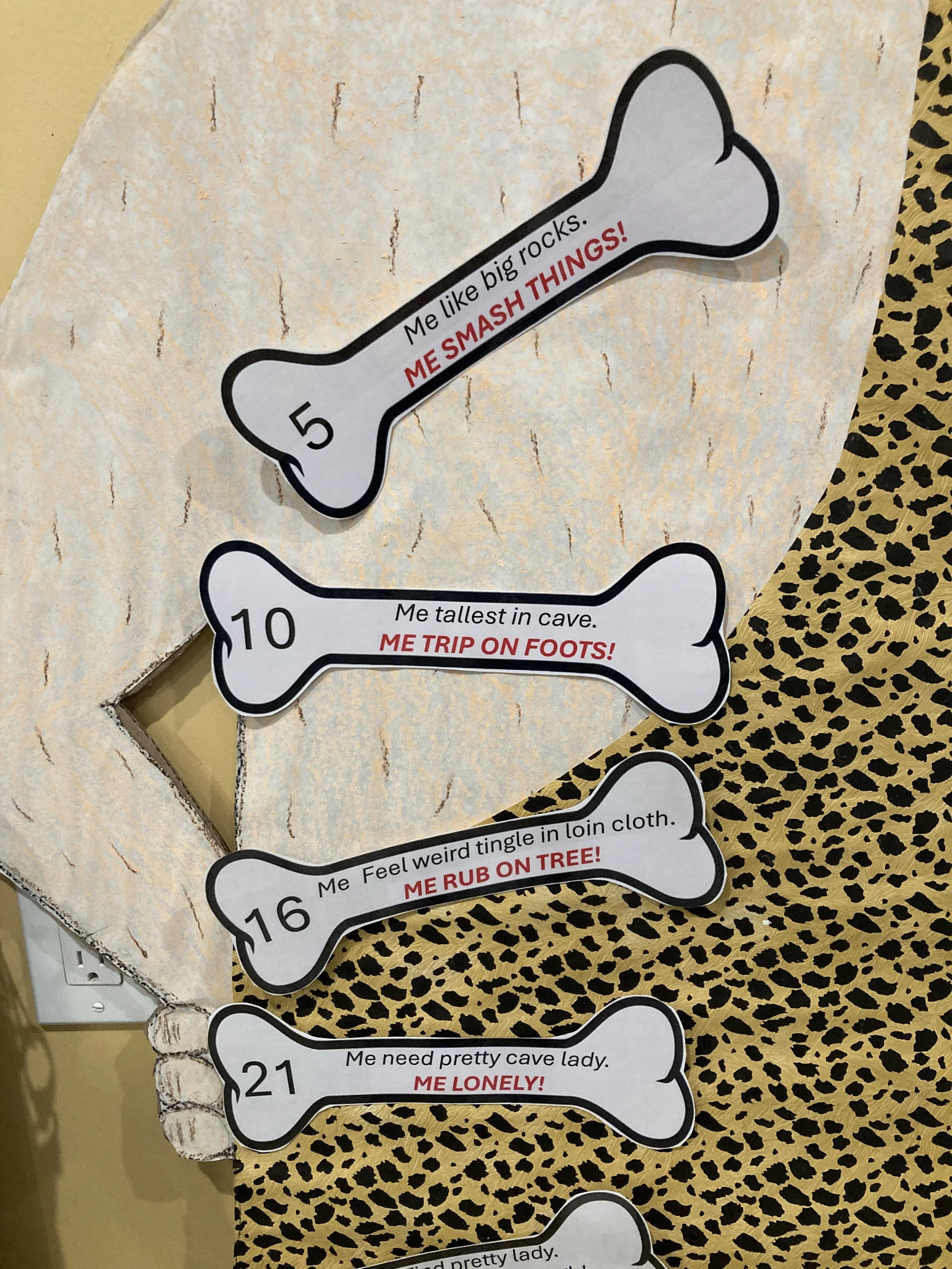 A paper cutout shaped like a dog bone with the number 5 on it. The cutout contains the message, "Me like big rocks. ME SMASH THINGS!" in red text.