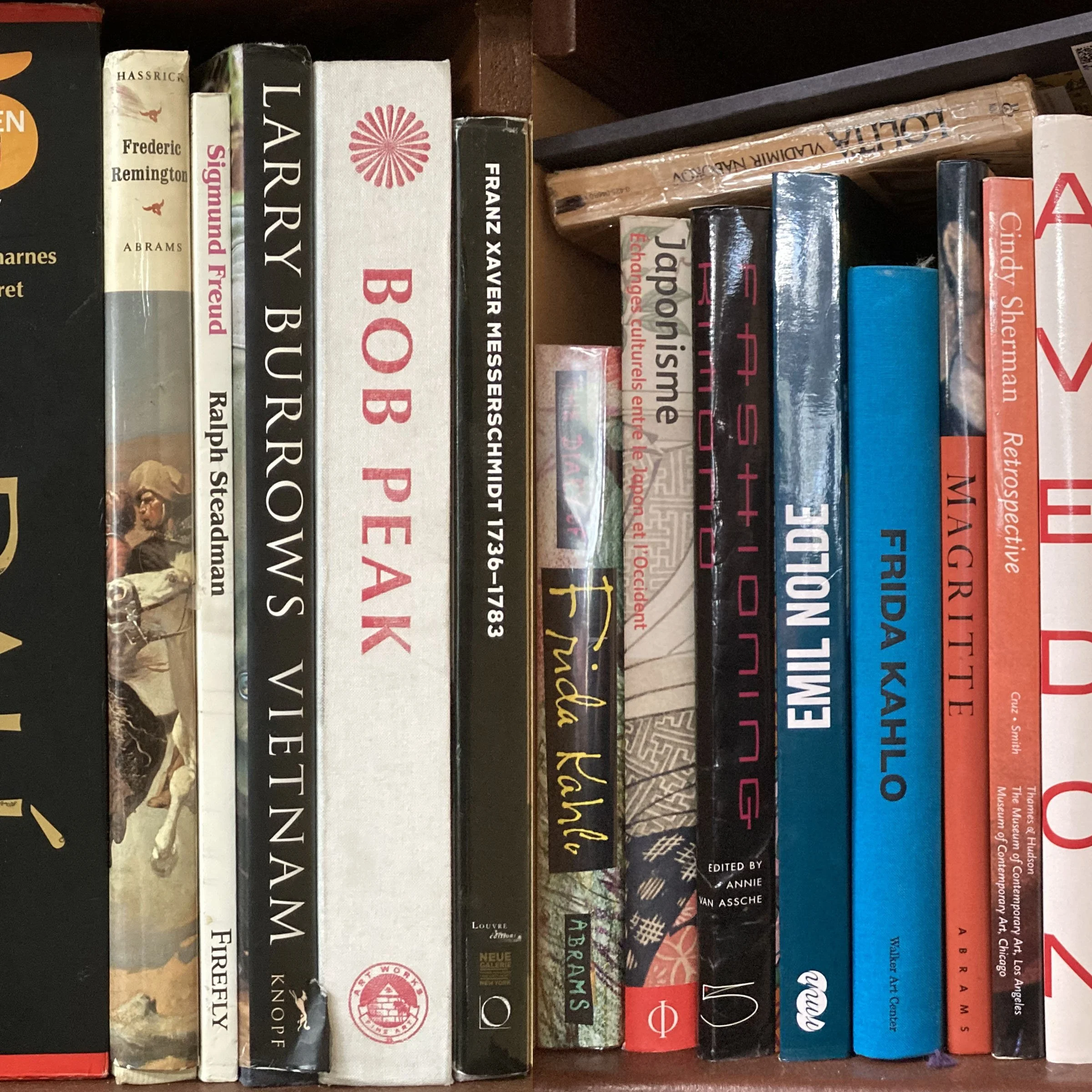 Close-up of a bookshelf with various hardcover books in different colors and sizes, including titles like 'Frederic Remington,' 'Arundel,' 'Franz Xaver Messerschmidt,' and 'Japonisme.'