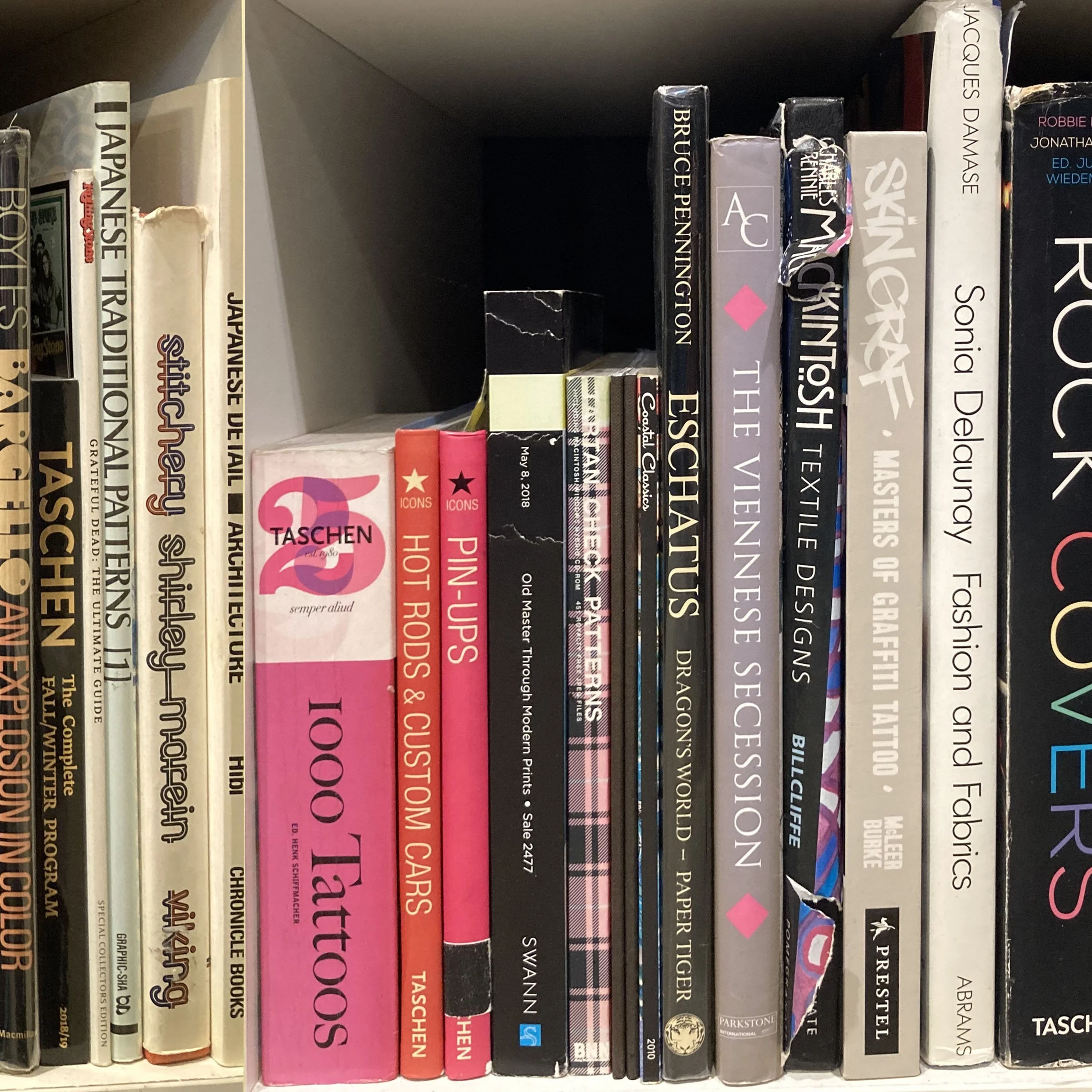 Bookshelves filled with various books, including titles on design, architecture, and art, with some books stacked horizontally and others standing vertically.