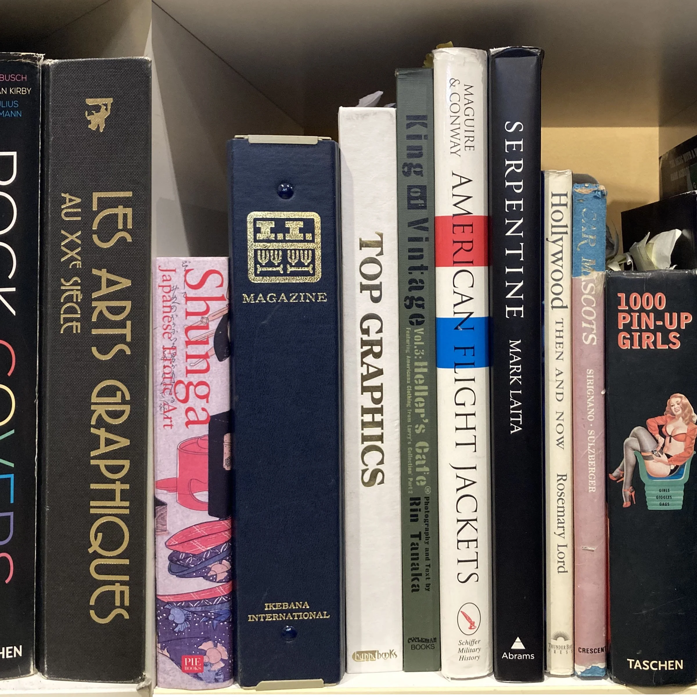 A bookshelf with various books, some titles include 'LE S A T', 'PIE', 'IKABANA INTERNATIONAL', 'Schiffer Military History', and 'Crescent'.