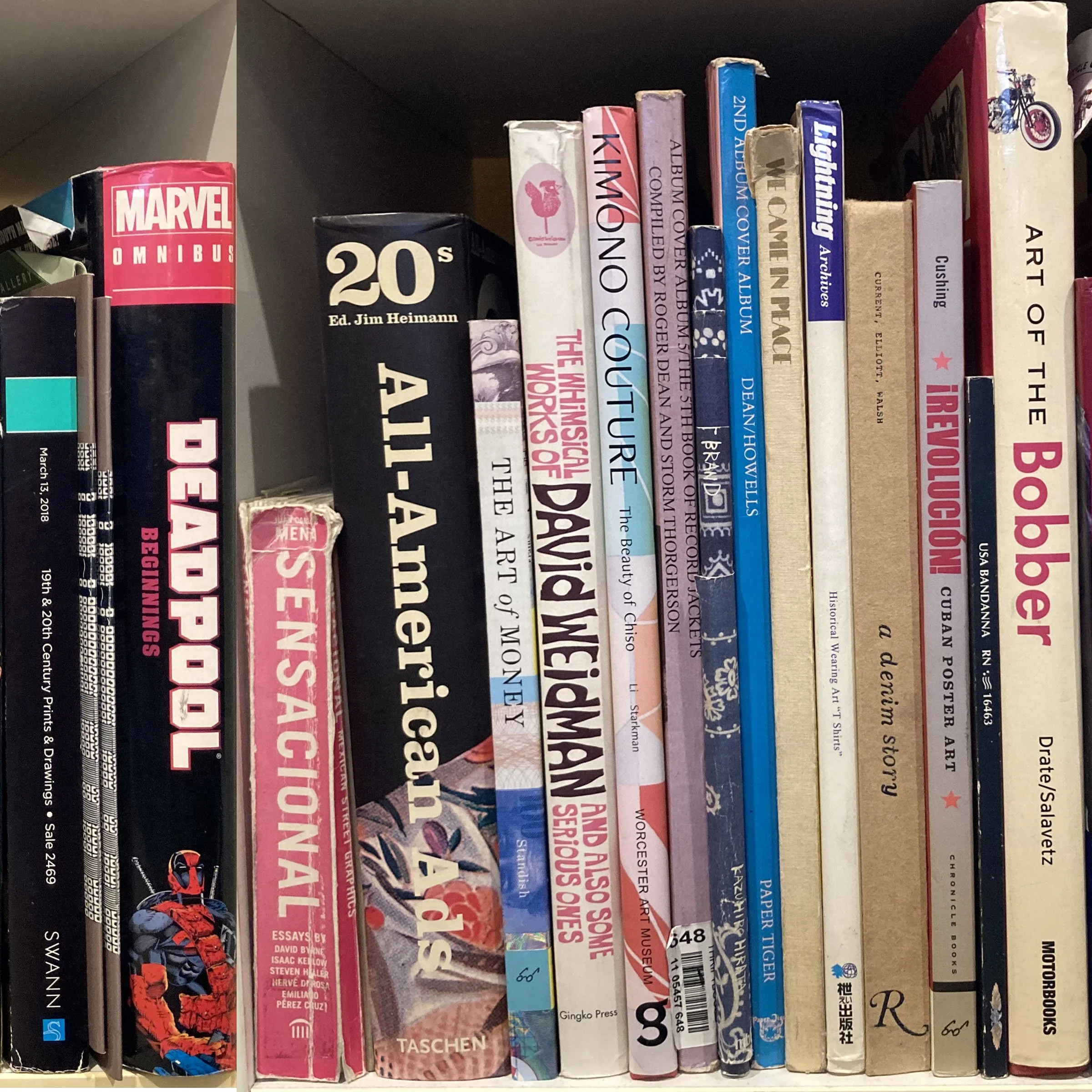 A shelf filled with various books of different sizes and colors, including titles related to art, history, and comic books, with some books showing partial titles and authors.