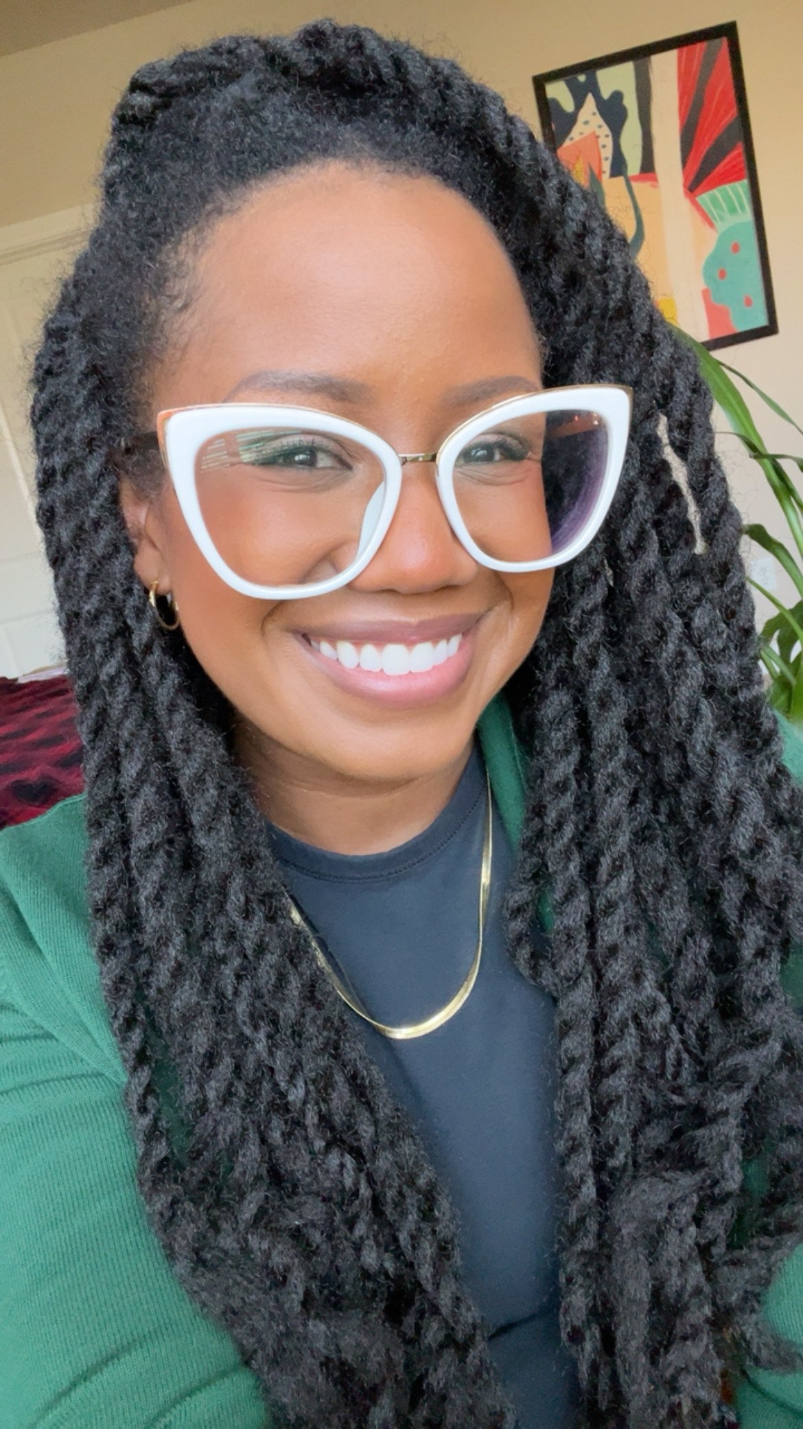 Picture of Robin smiling wearing long Marley twists, white glasses, and a green sweater