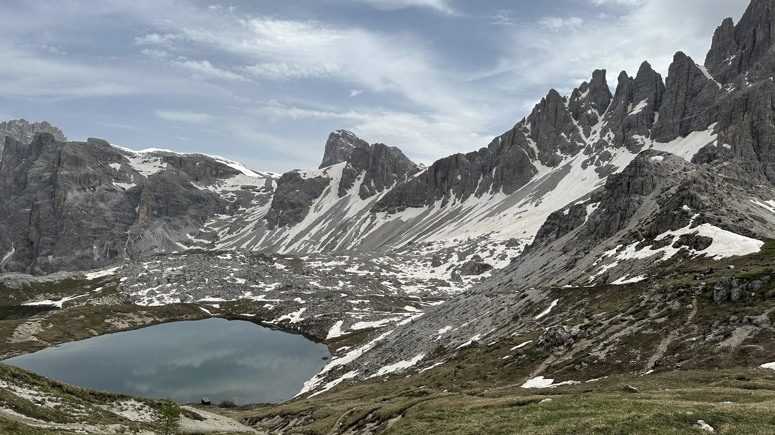 A mountain landscape with snow-capped peaks, a small lake in the foreground, and partly cloudy sky.